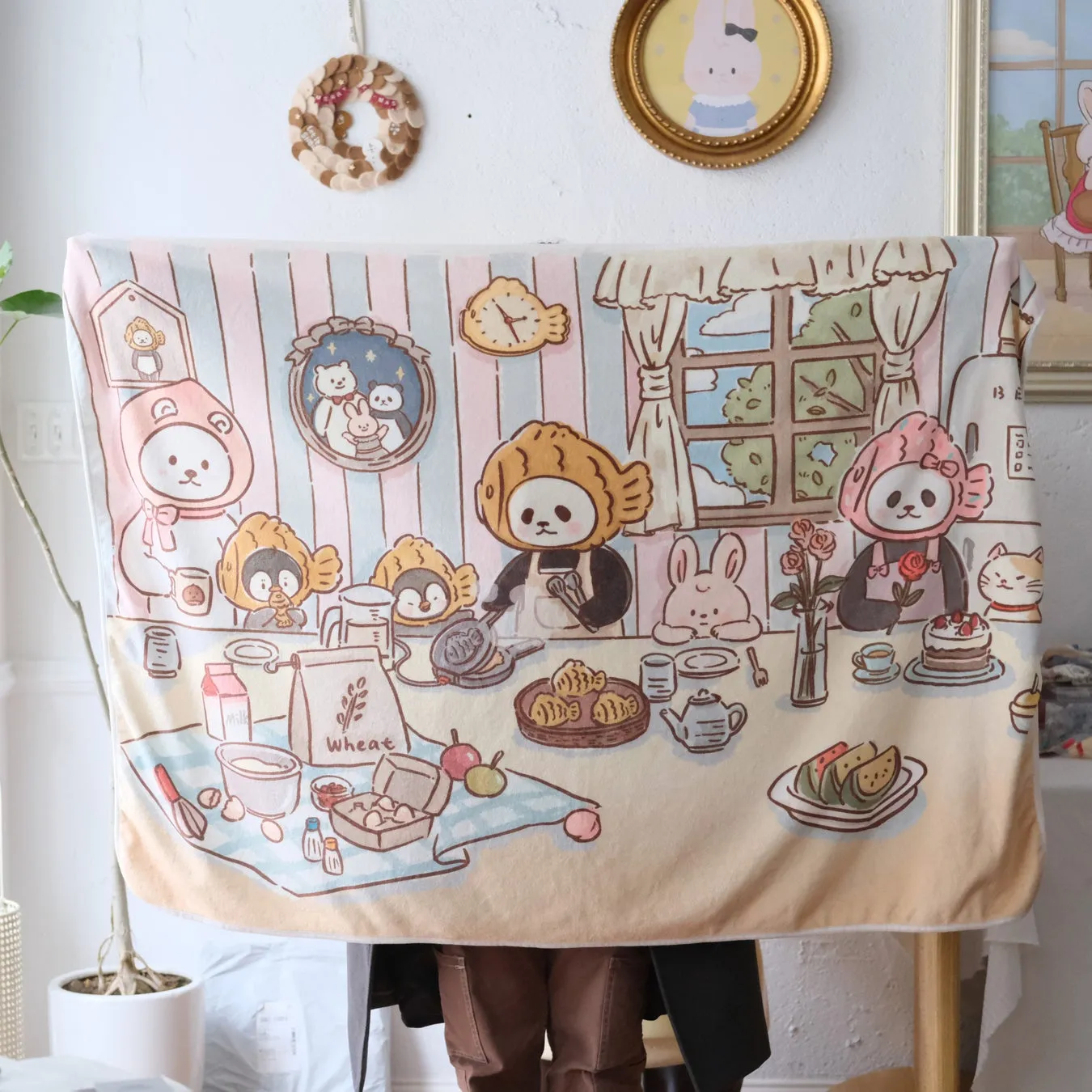 可愛らしい動物たちがパンケーキを作っているイラストが描かれたタオル。周囲には、壁に飾られた絵や装飾が見える。