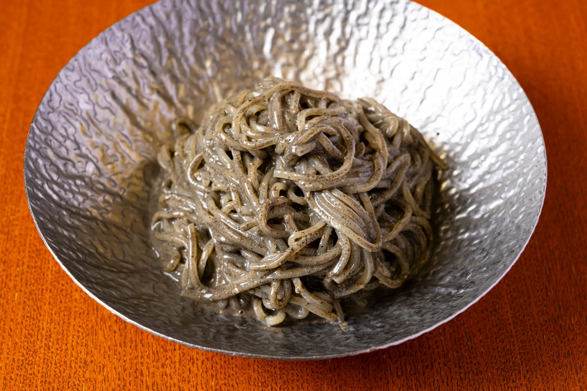 銀色の器に入った麺料理のクローズアップ写真。麺はグレーで、器は金属のような質感。