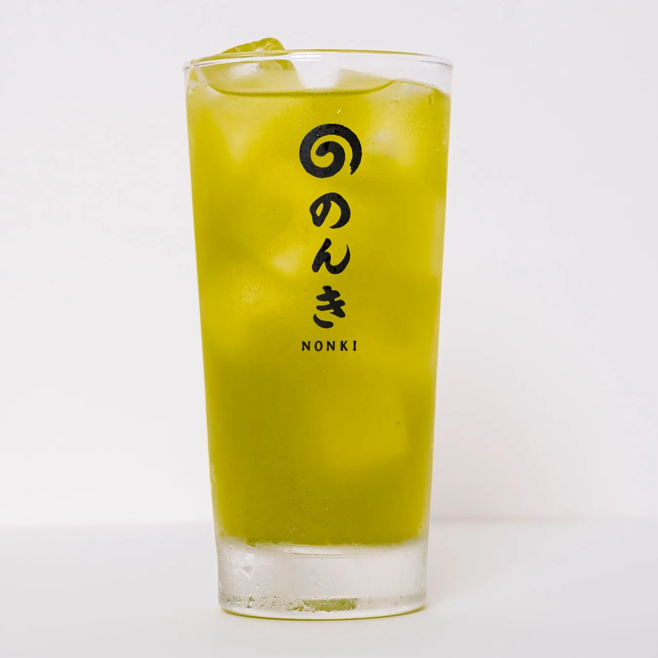 グラスに入った抹茶のような緑色のドリンク。氷が入っており、ロゴが印字されている。