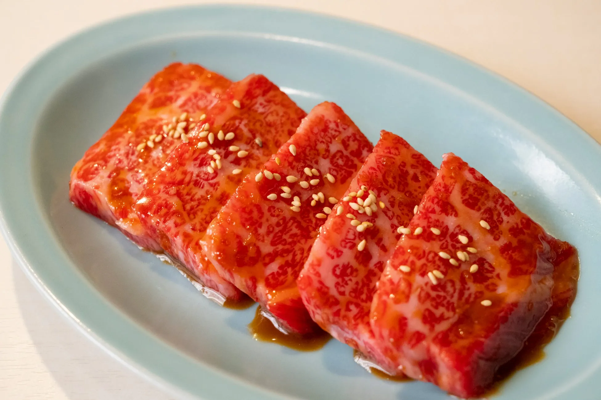 お皿に盛られた、霜降りの牛肉のアップです。牛肉はカットされ、醤油ベースのタレが塗られ、白ごまが散らされています。