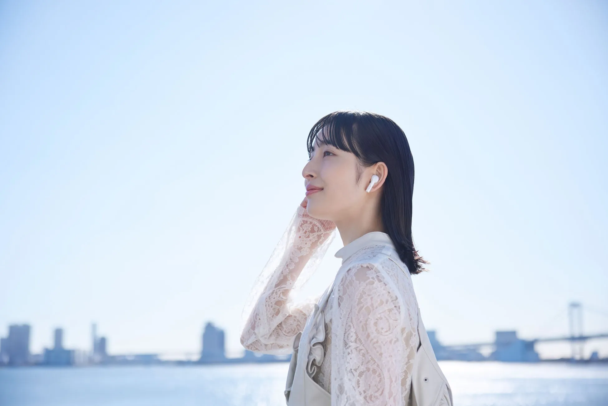 イヤホンを装着した女性が屋外で空を見上げている様子。