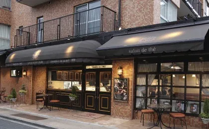 カフェの外観。黒いひさしに「salon de thé」の文字が見える。レンガ造りの建物で、テラス席もある。