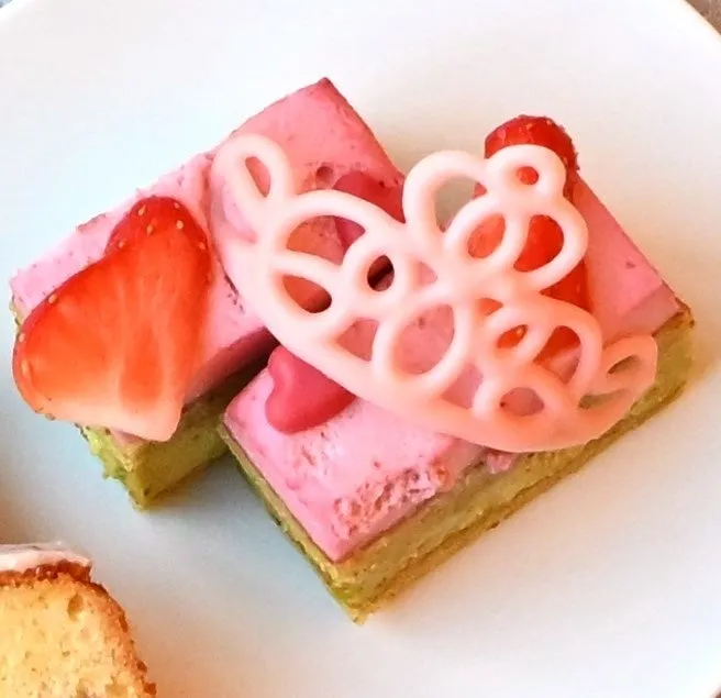 ピンク色のケーキが2つ、白い皿の上に置かれています。ケーキの上には、ハート型のイチゴのスライスと、ピンク色の装飾が施されています。