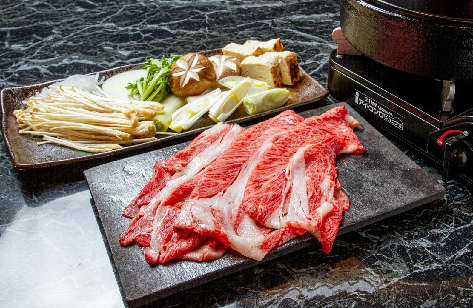 和食のすき焼きの材料を写した写真。牛肉、野菜、きのこ、豆腐など、さまざまな食材が写っています。