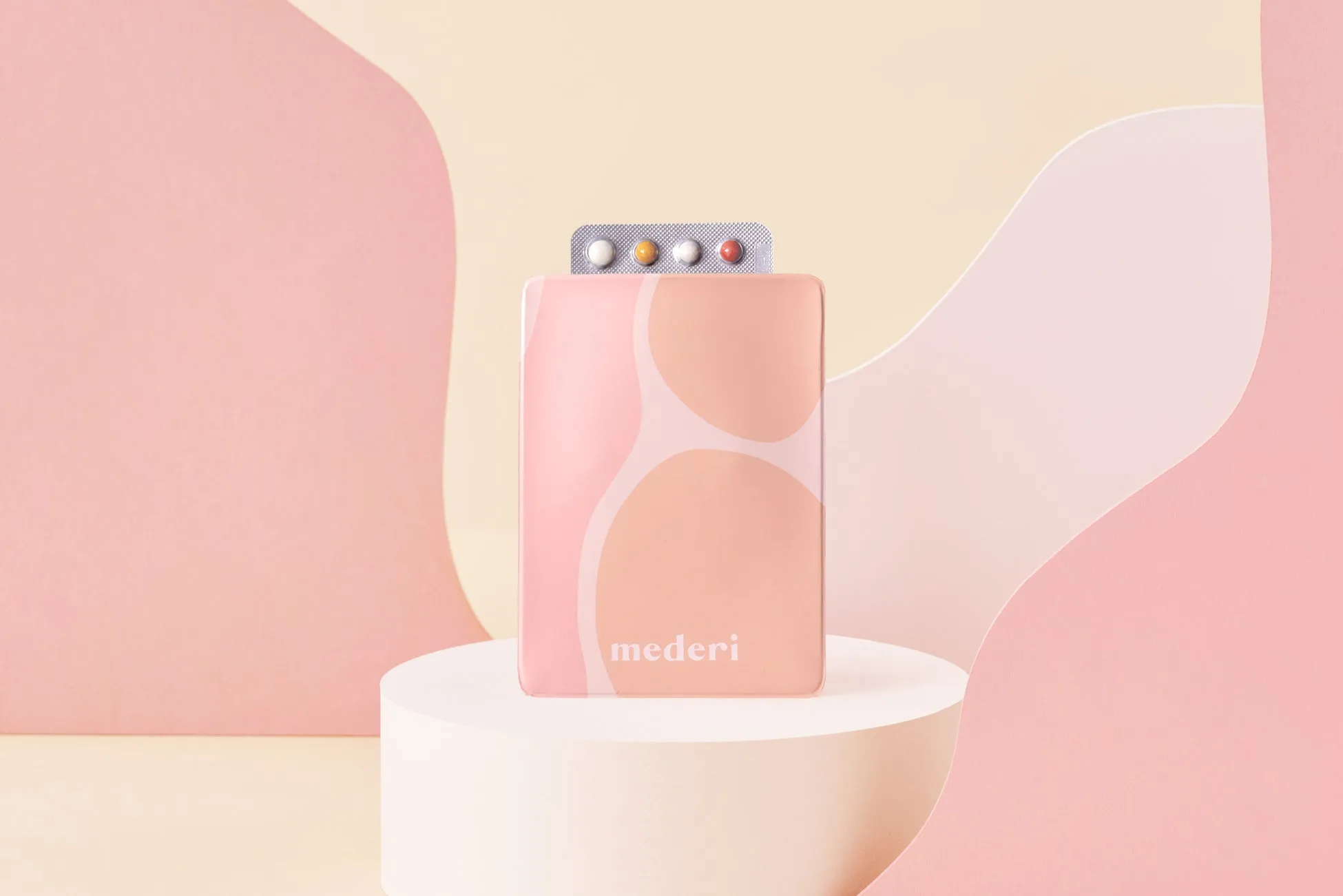 ピンク色の背景に、薬が入ったピンク色のケースが置かれています。ケースの上には、4つの色の薬が入ったブリスターパックが部分的に見えています。mederiのロゴがケースに表示されています。