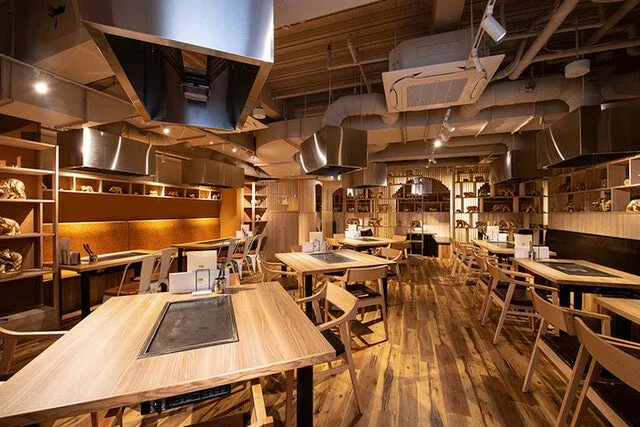 木材を基調としたスタイリッシュな雰囲気の店内。テーブル席が並び、天井には排気ダクトが設置されている。