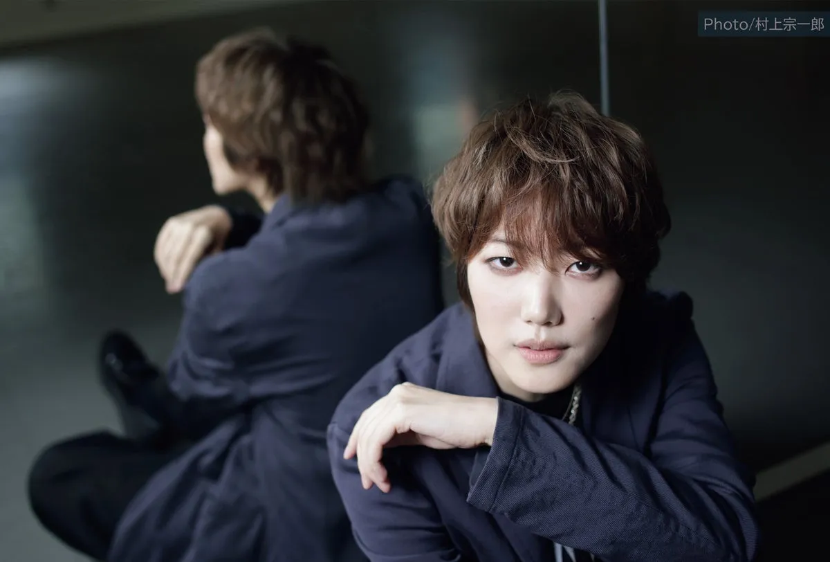 男性がこちらを真っ直ぐ見つめている写真。背景には男性の姿が鏡のように映っている。