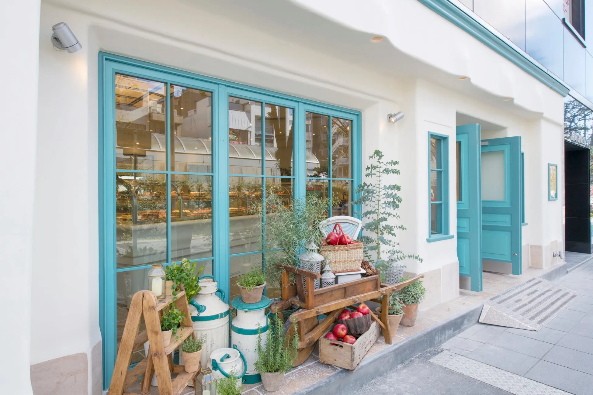 お店の入り口の画像。青い窓とドアが特徴で、店の前にはリンゴや植物が飾られている。