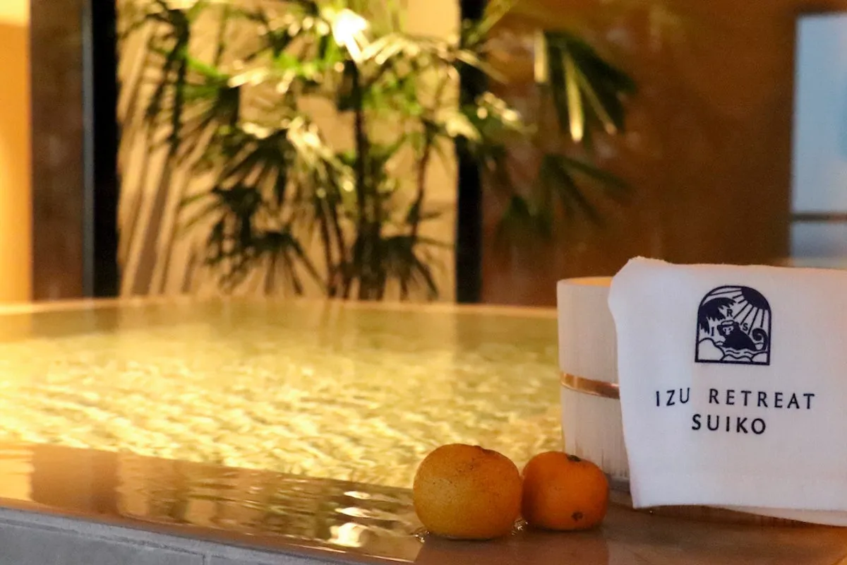 温泉の湯船にみかんが浮かび、タオルには「IZU RETREAT SUIKO」のロゴが