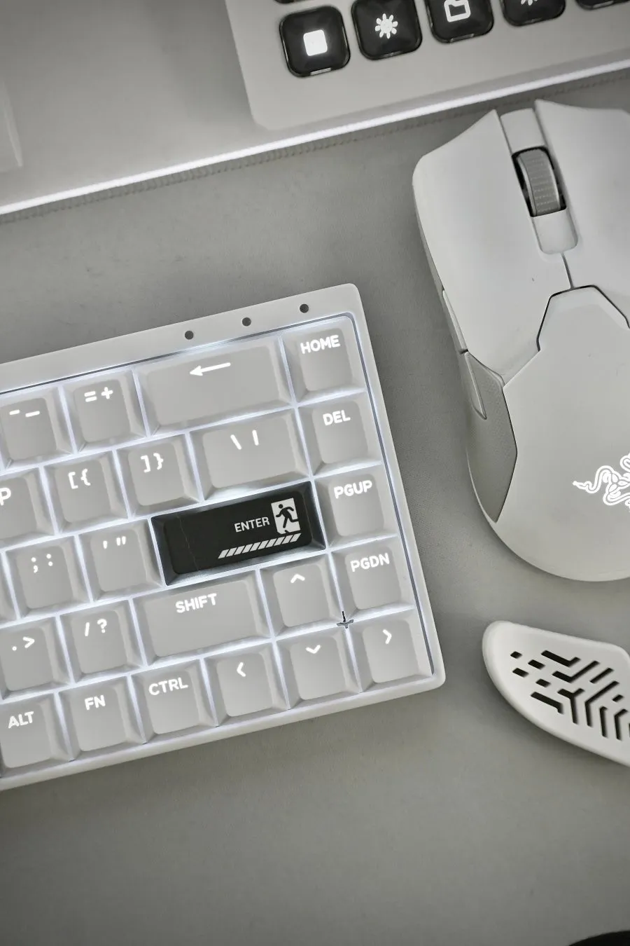 白いキーボード、マウス、マウスパッドが写った写真です。キーボードのEnterキーには、人が出口に向かって歩いているようなアイコンが描かれています。マウスはRazerのものである。