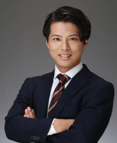 ネイビーのスーツを着て腕を組んで微笑んでいるアジア系の男性のポートレート。