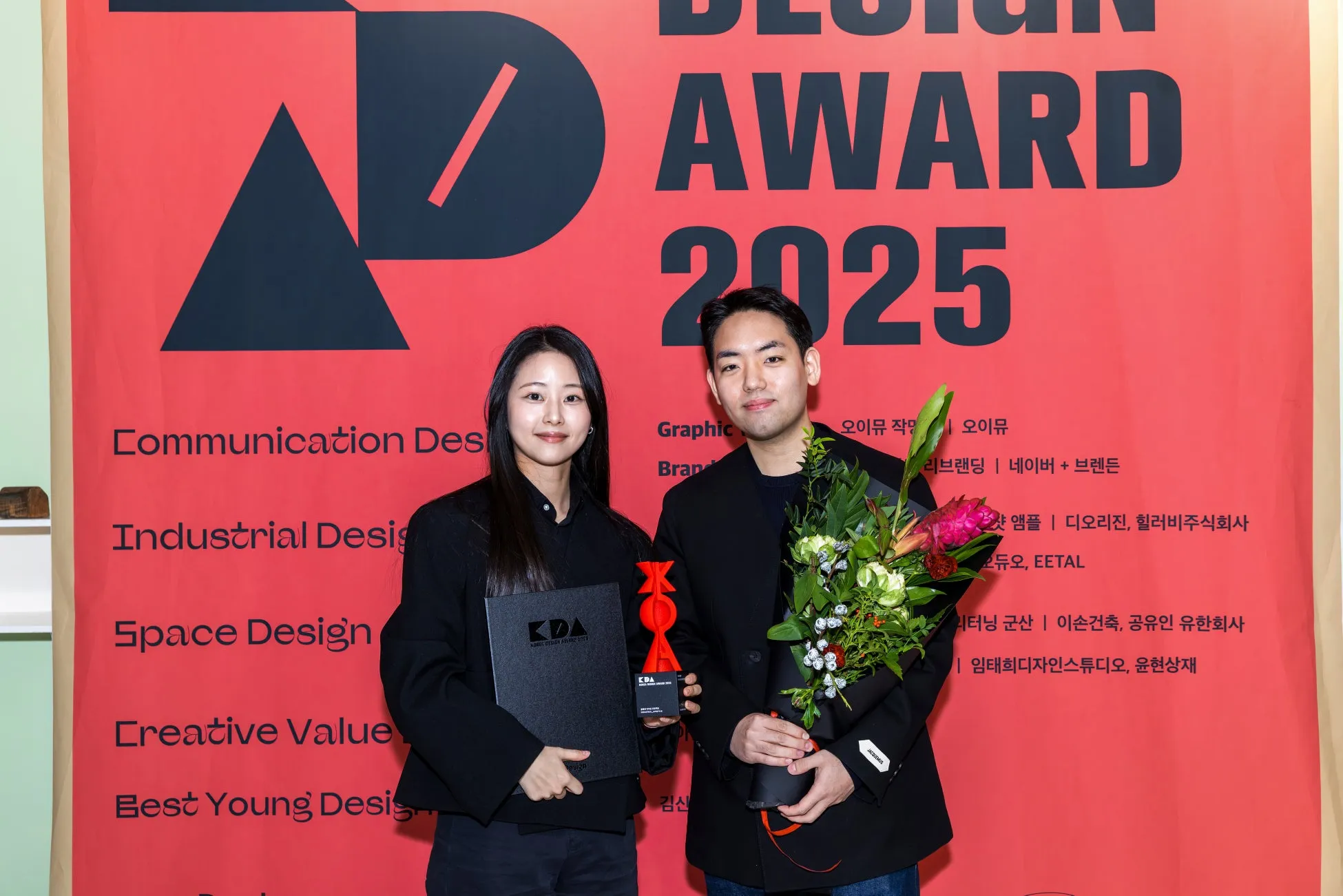 トロフィーと花束を持つ男女の写真。受賞の喜びが伝わる一枚。