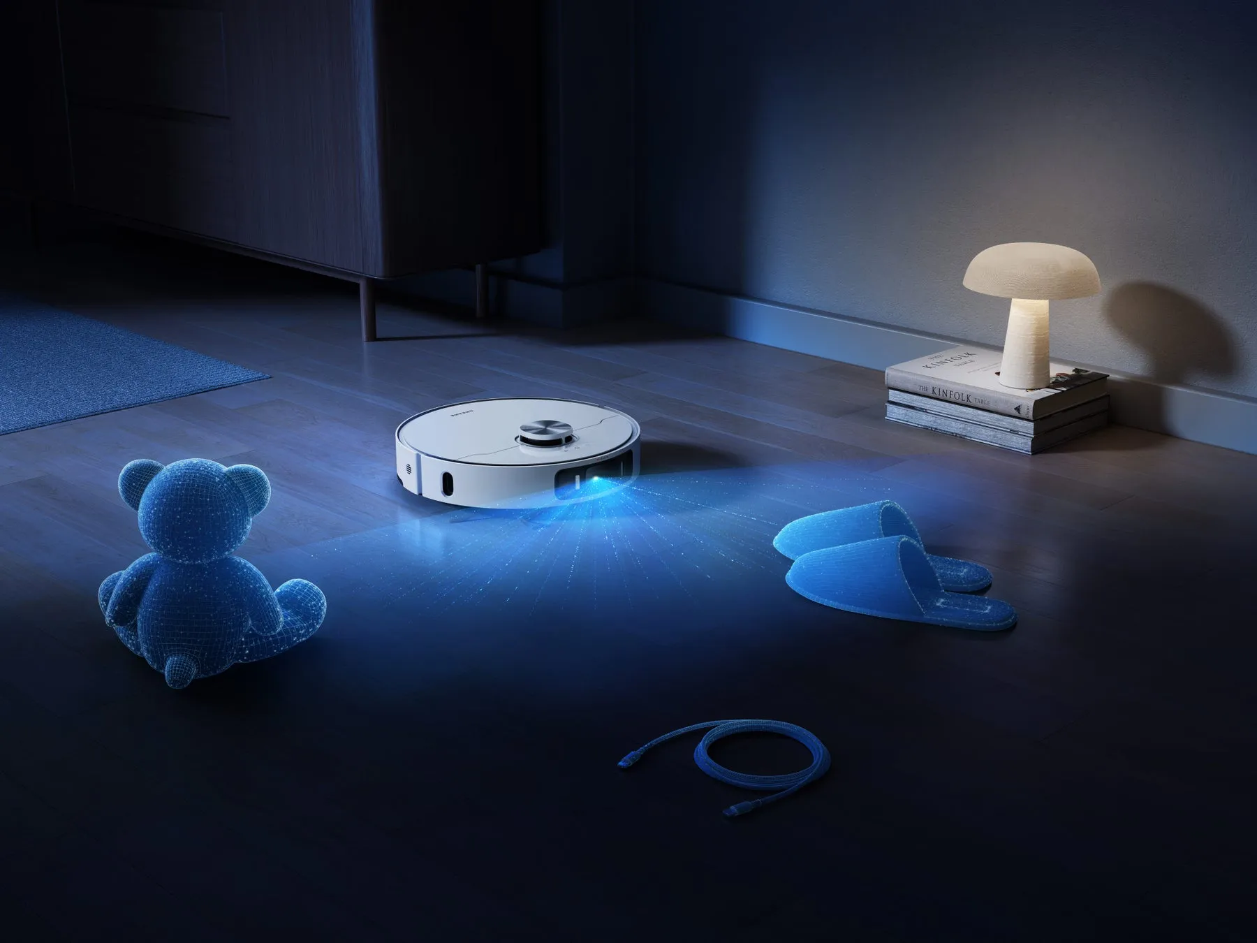 夜の部屋で、ロボット掃除機が床を掃除している様子。床には、クマのぬいぐるみ、スリッパ、ケーブル、本が置かれている。