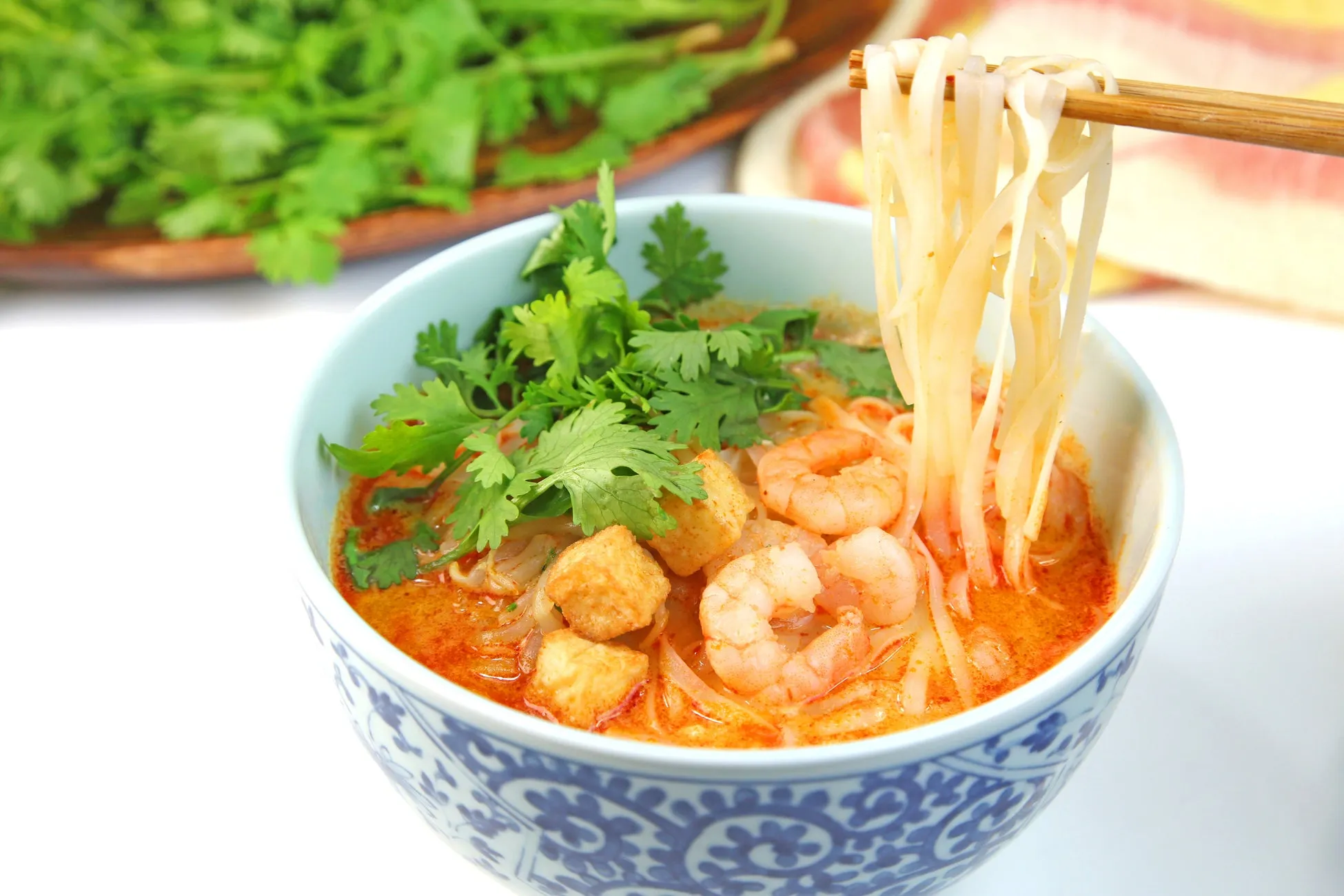 エビと豆腐が入ったラクサのクローズアップ写真。箸で麺を持ち上げている。