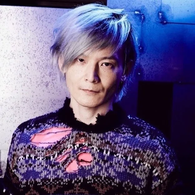 銀髪の男性のポートレート。彼は黒と青のセーターを着ており、カメラ目線で微笑んでいる。