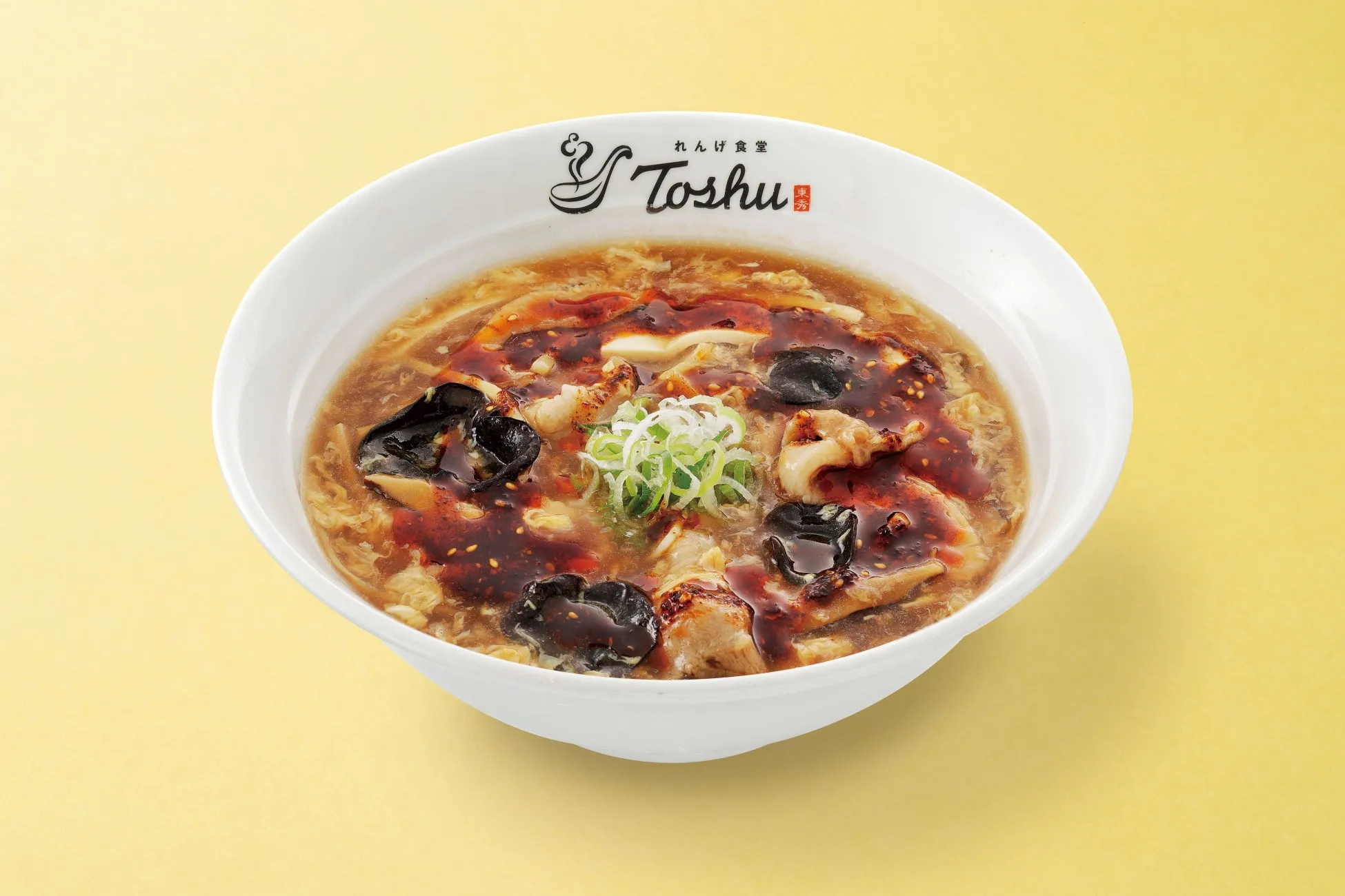 白い器に入った中華料理の画像です。料理は、黒いキクラゲやネギがトッピングされた、茶色いスープです。スープの上には、赤いラー油のようなものがかかっています。