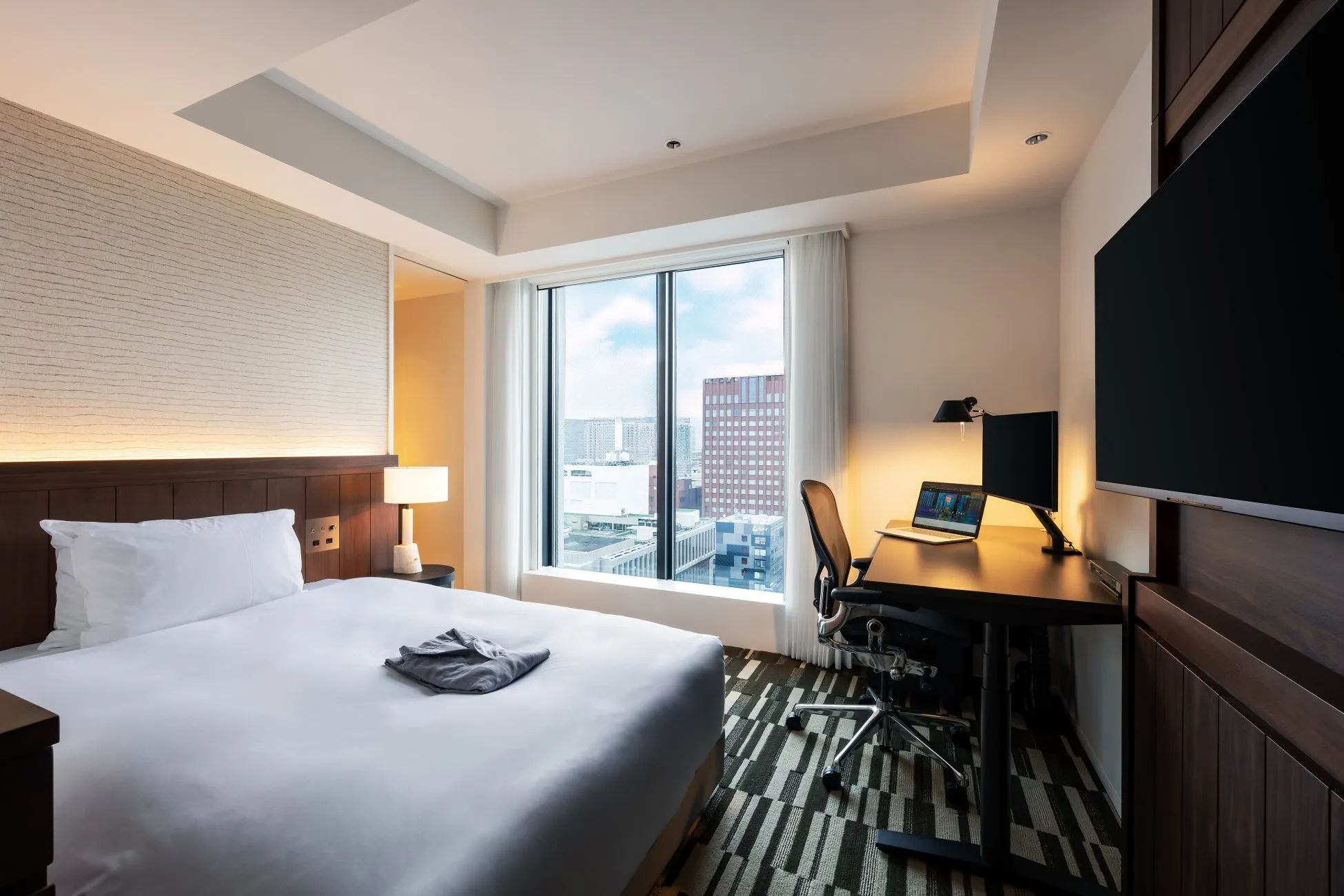 ホテルの客室。ベッド、デスク、窓、テレビが写っている。