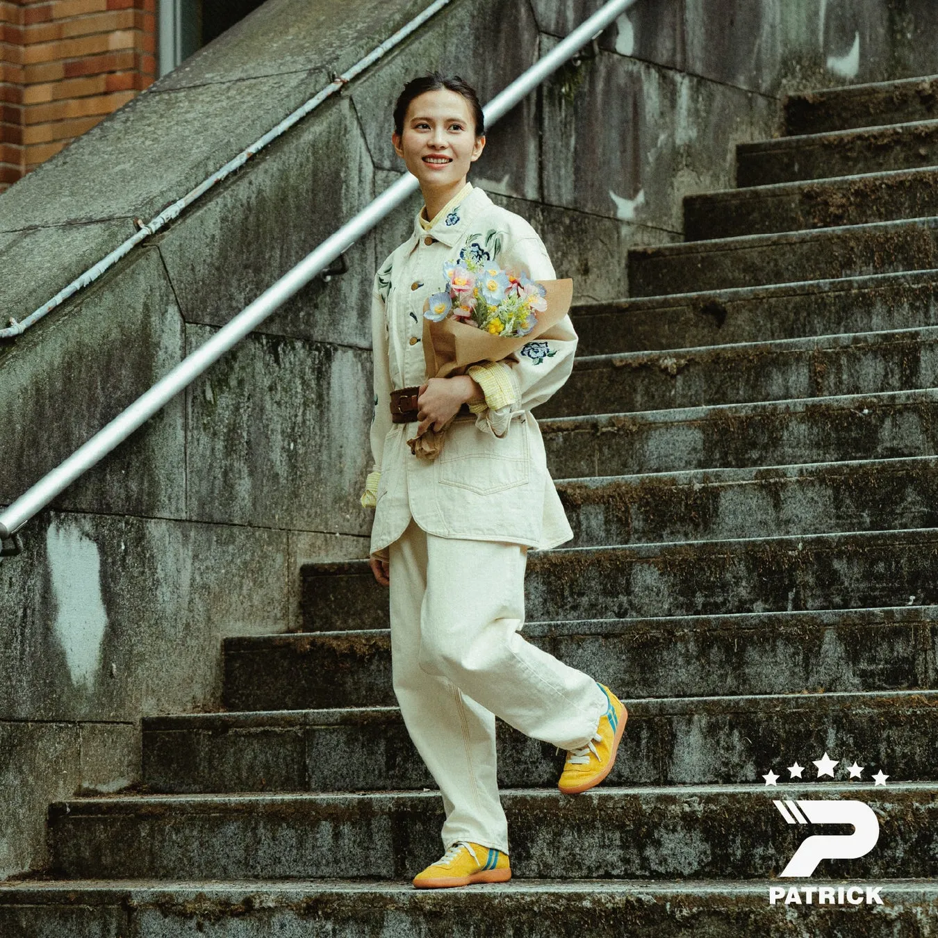 階段を降りる女性が、花束とスニーカーを持っている様子