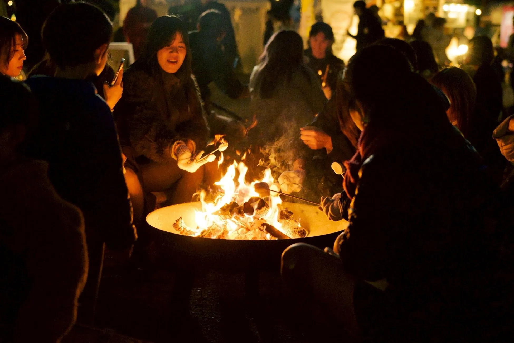 焚き火を囲んでマシュマロを焼いている人々の様子。