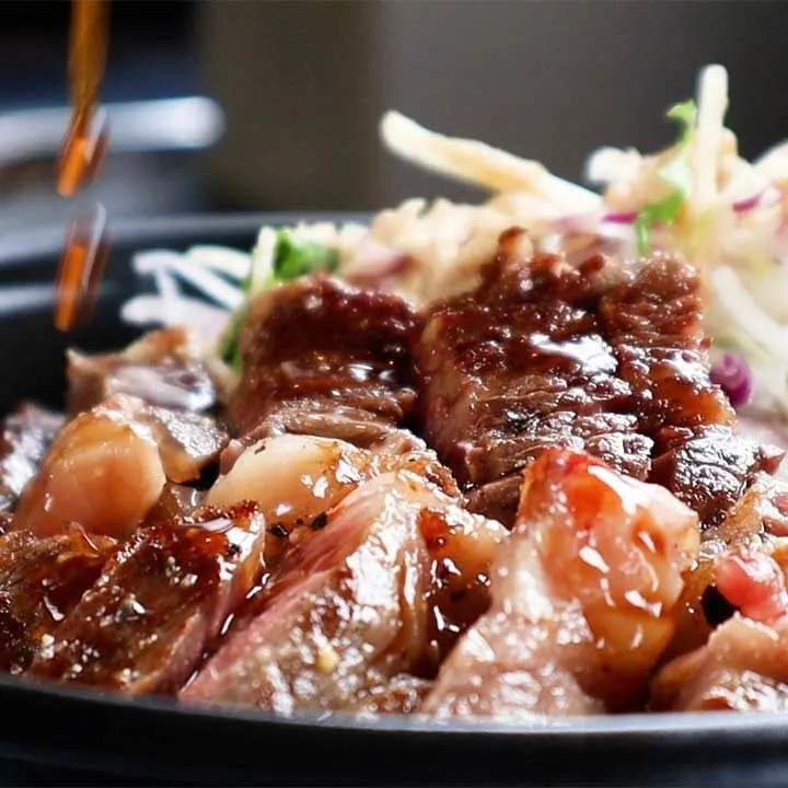 ステーキにソースをかけている写真。サラダも添えられている。