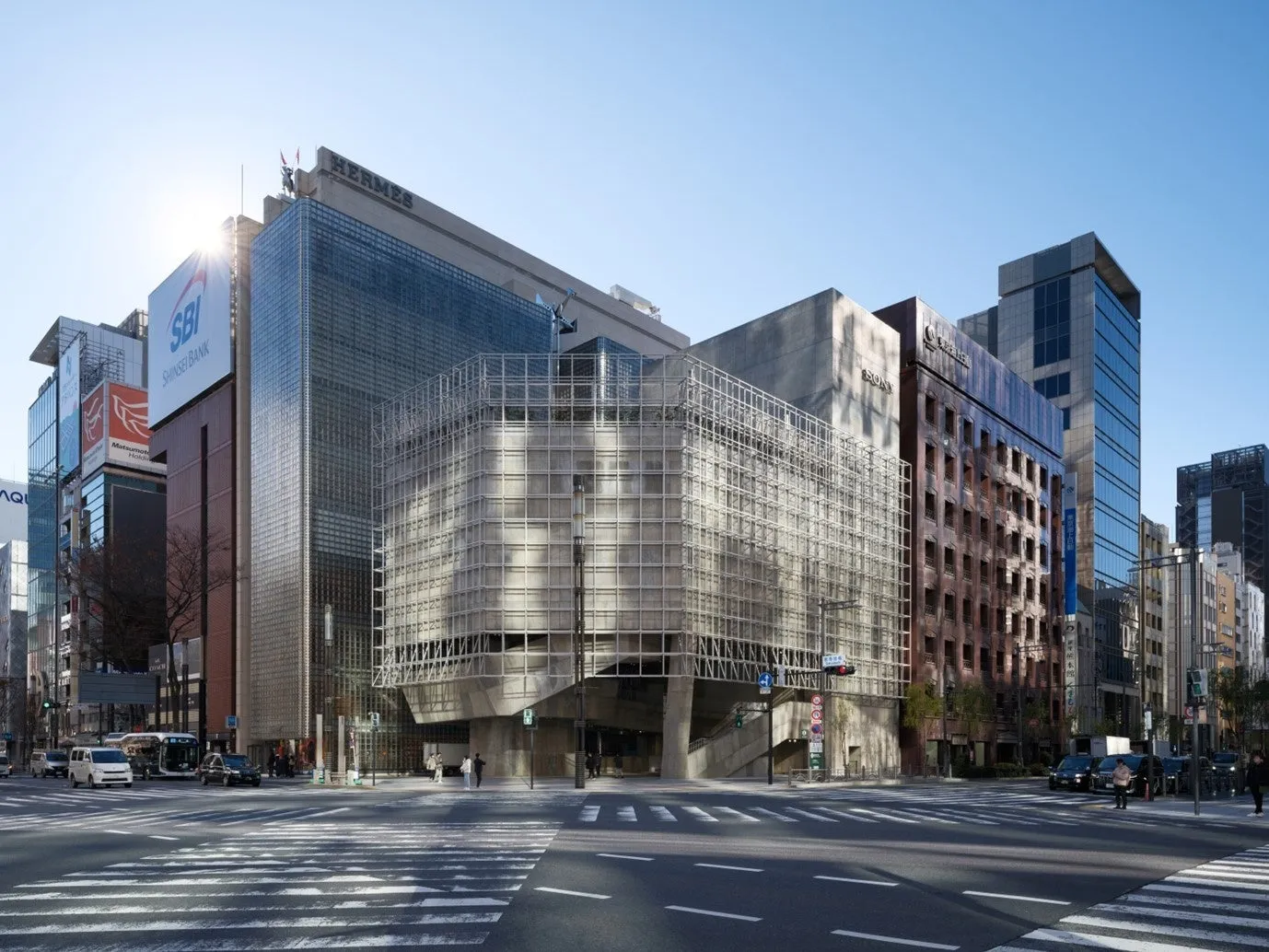 晴れた日の街並みの写真。交差点に面した複数の高層ビルが写っています。左側のビルには「SBI Shinsei Bank」の看板があり、その上のビルには「HERMES」の文字が見えます。右側のビルには「SONY」の文字が見えます。横断歩道を歩く人々や、車も写っています。