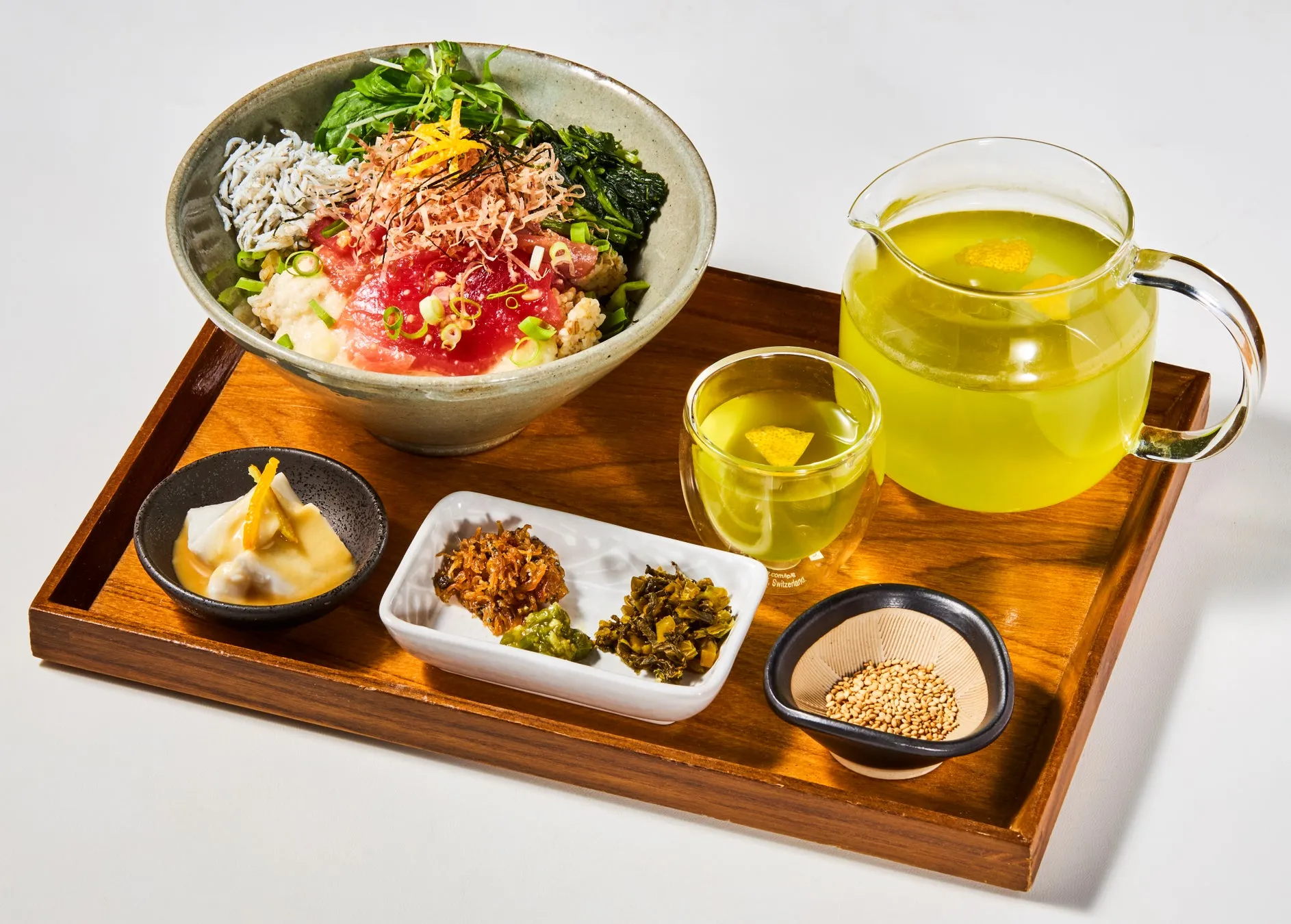 木製のトレーに、マグロ丼、漬物、ごま、お茶などが盛り付けられた日本の食卓の様子。