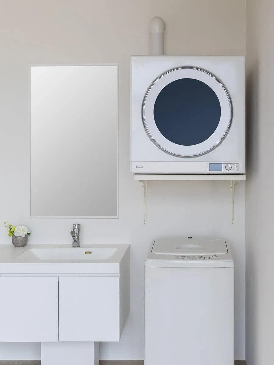 白を基調とした洗面所。壁に設置された洗濯乾燥機、洗面台、洗濯機が配置されている。