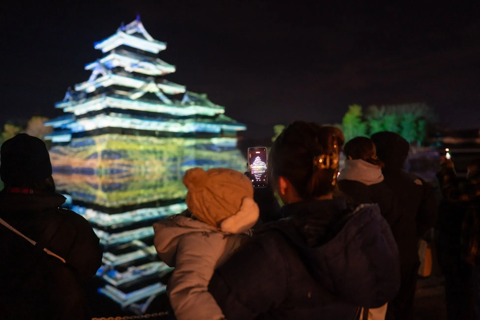 夜にライトアップされたお城を撮影する人々