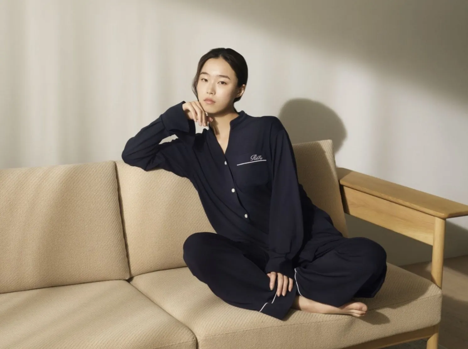 女性が紺色のパジャマを着て、ベージュのソファに座ってくつろいでいる写真です。