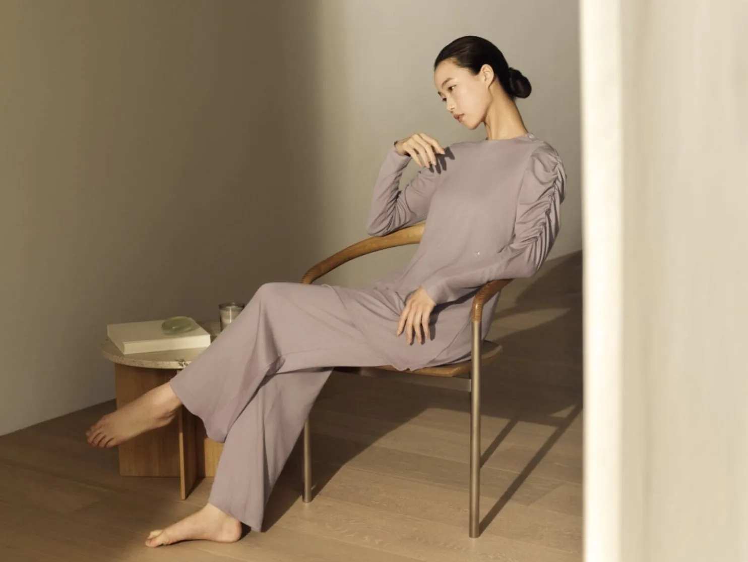 女性が椅子に座ってくつろいでいる様子。彼女はラベンダー色のセットアップを着ており、髪はまとめられています。