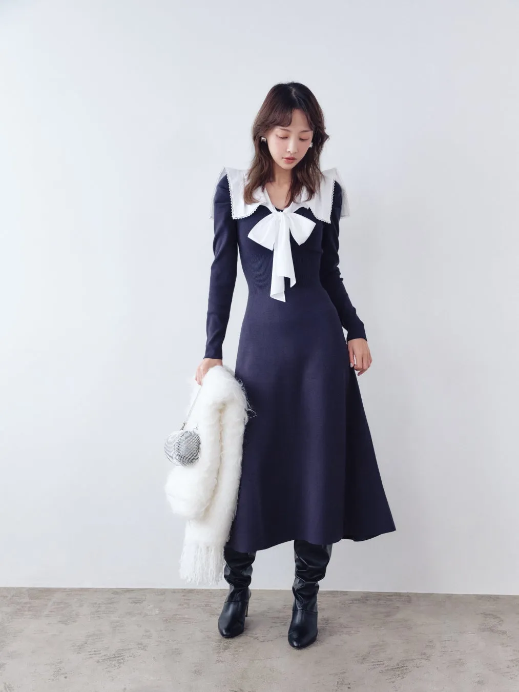 女性がネイビーのワンピースを着て、白いファーのマフラーと小さなバッグを持っています。