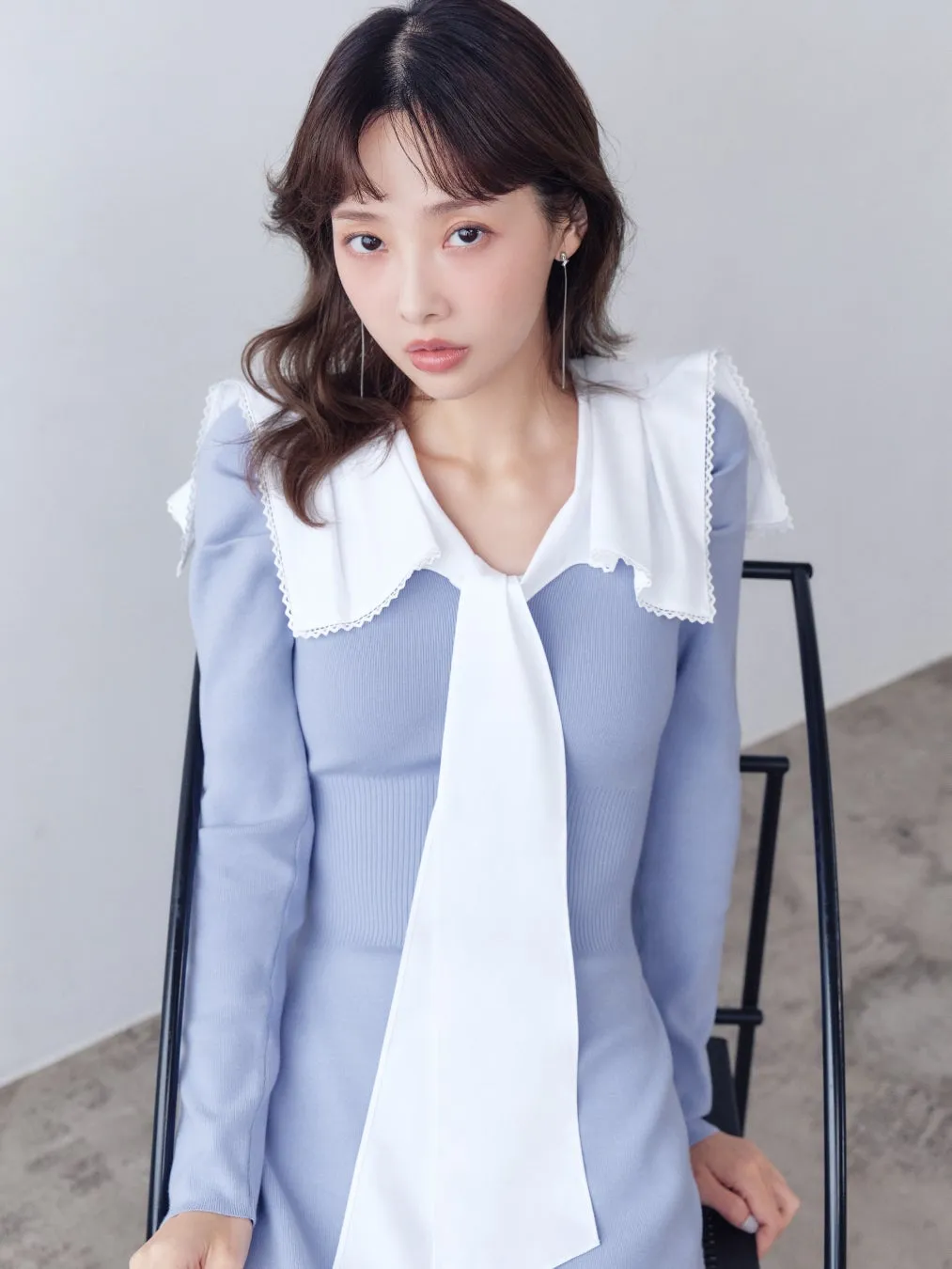 女性が椅子に座ってカメラを見つめている水色のニットワンピースの女性