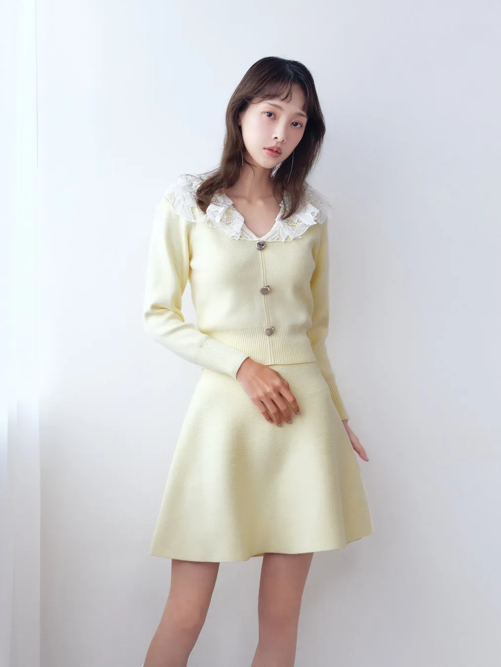 女性が、黄色いカーディガンとスカートのアンサンブルを着て立っている写真