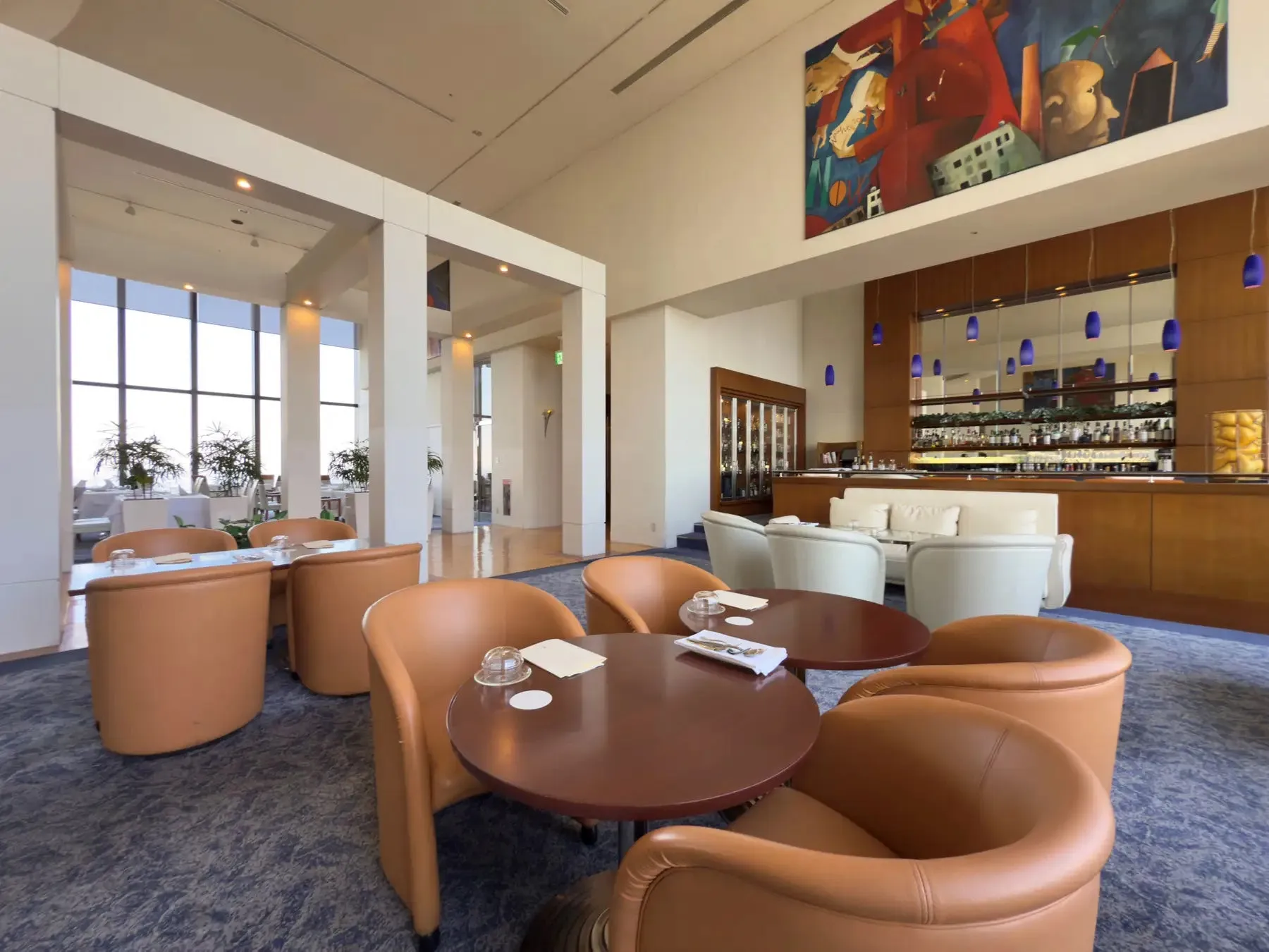 モダンな雰囲気のラウンジのインテリア。革張りの椅子と丸テーブルが配置され、奥にはバーカウンターとアート作品が飾られている。