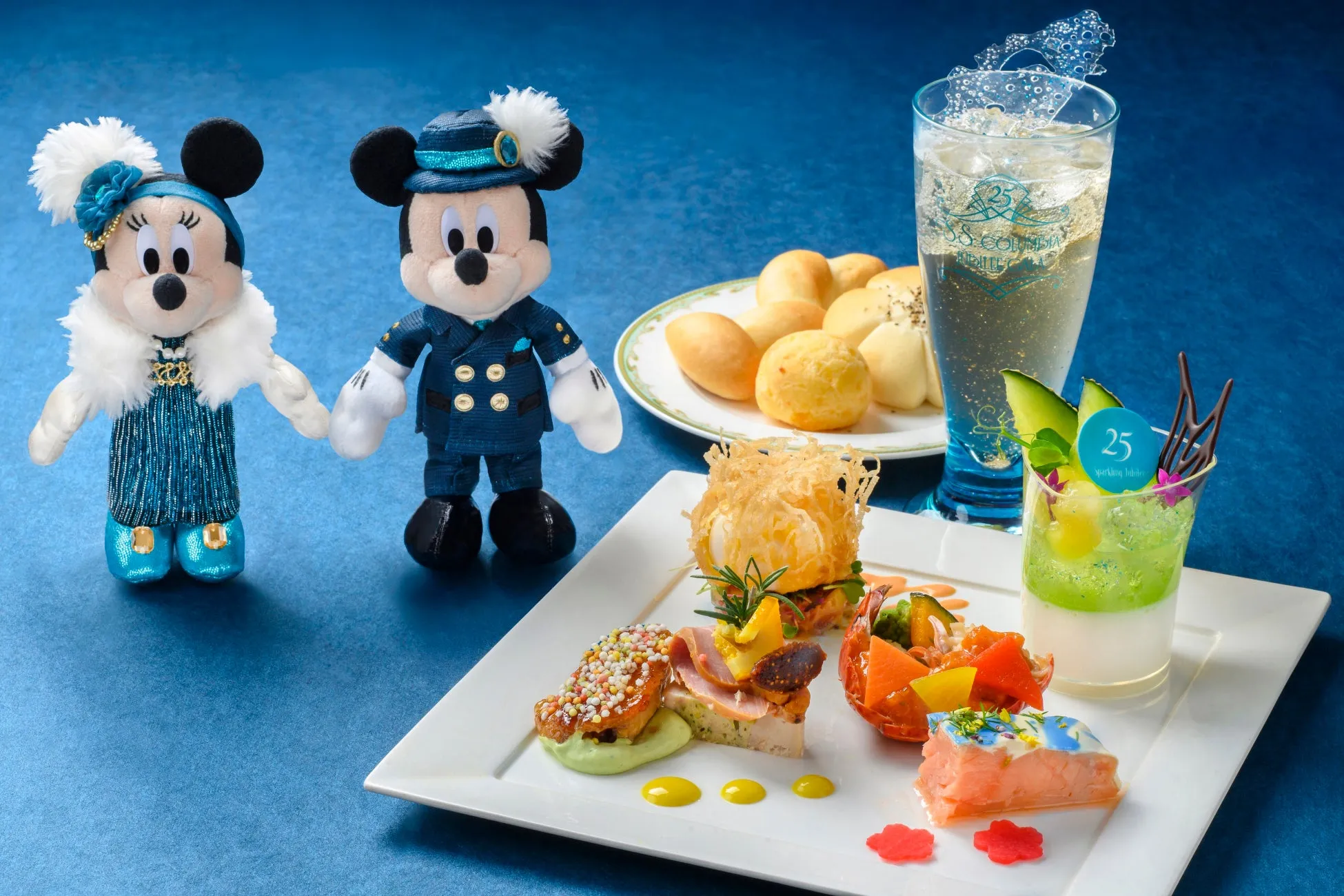 ミッキーとミニーのぬいぐるみと、コース料理が写った写真。コース料理には、パン、ドリンク、前菜、デザートなどが含まれている。