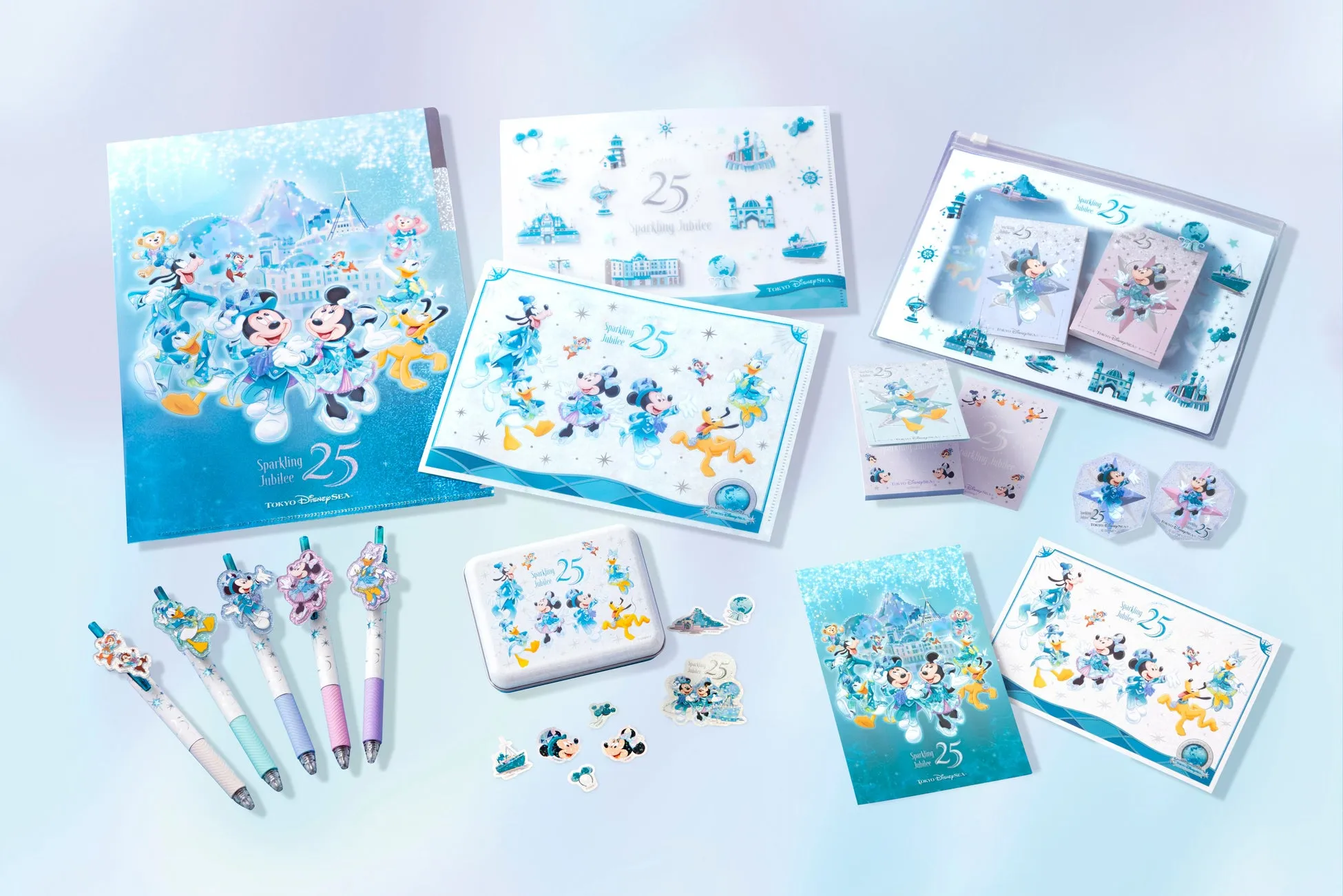 東京ディズニーシー25周年記念のグッズが並んだ写真。ミッキーマウス、ミニーマウス、ドナルドダック、グーフィー、プルートなどのディズニーのキャラクターが描かれたファイル、メモ帳、ペン、ステッカー、缶バッジなど様々なアイテムがある。全体的に水色を基調としたデザインで、キラキラとした装飾が施されている。
