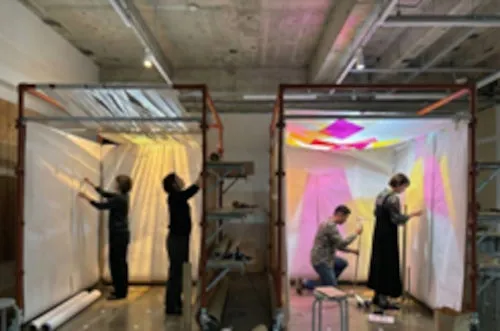 2つのフレームに囲まれた白い幕の中で作業をする人々の写真