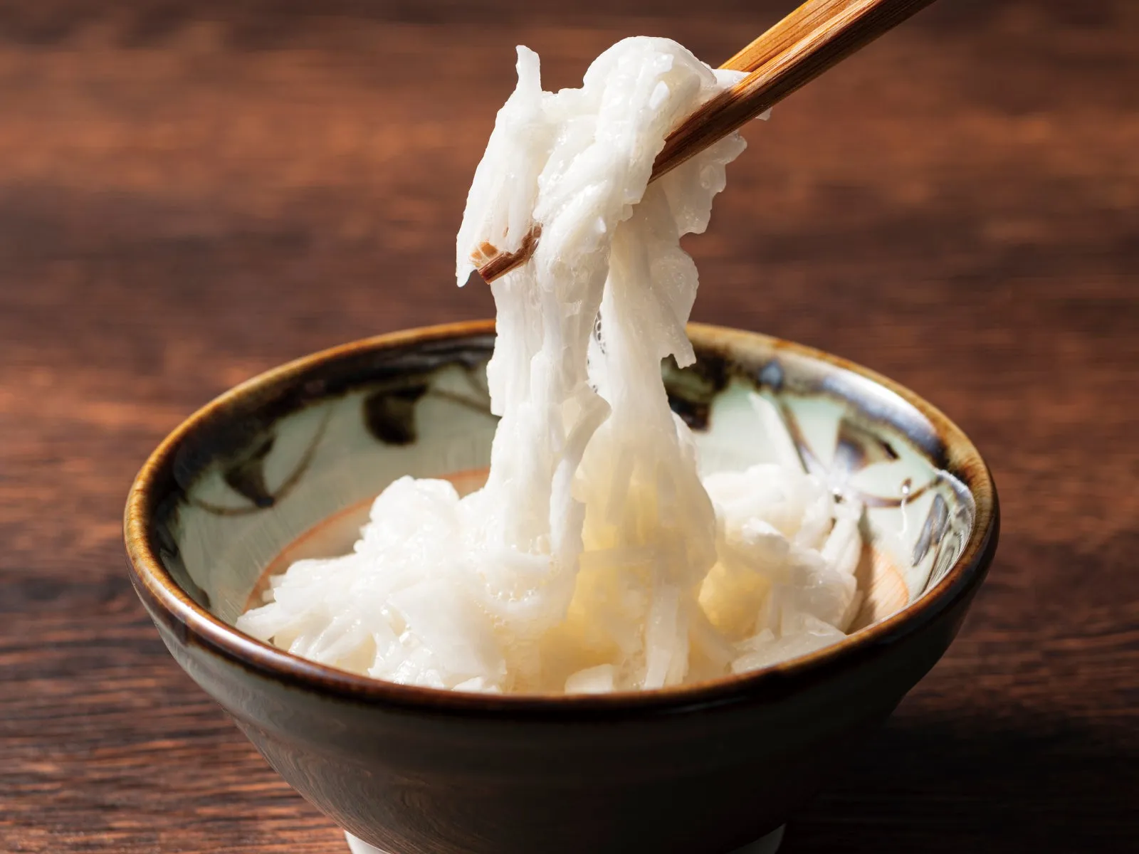 箸で持ち上げられた白く細長い麺が盛られた器のクローズアップ