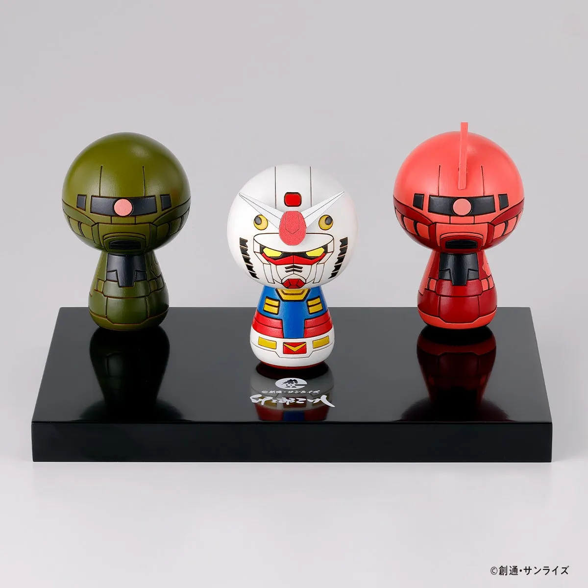 3体のガンダムのキャラクターを模した木製の置物が黒い台座に載せられている写真です。左から緑色のザク、真ん中にガンダム、右に赤いシャア専用ザクが配置されています。