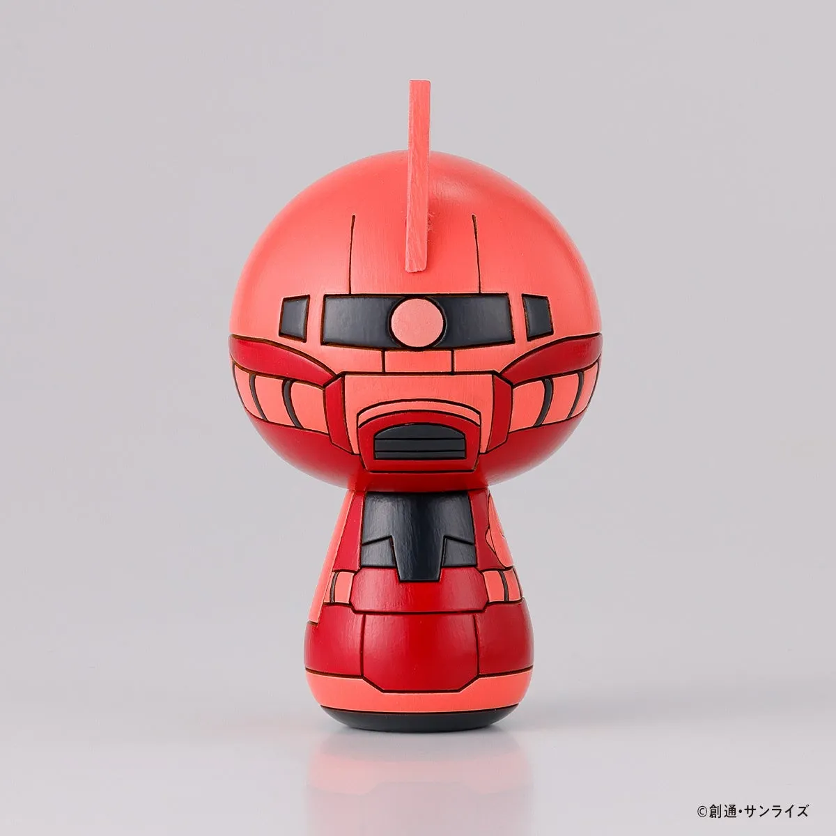 赤いロボットの置物。頭部と胴体で構成され、顔の部分は黒いパーツで縁取られている。頭頂部には突起があり、下部には黒いパーツが見える。