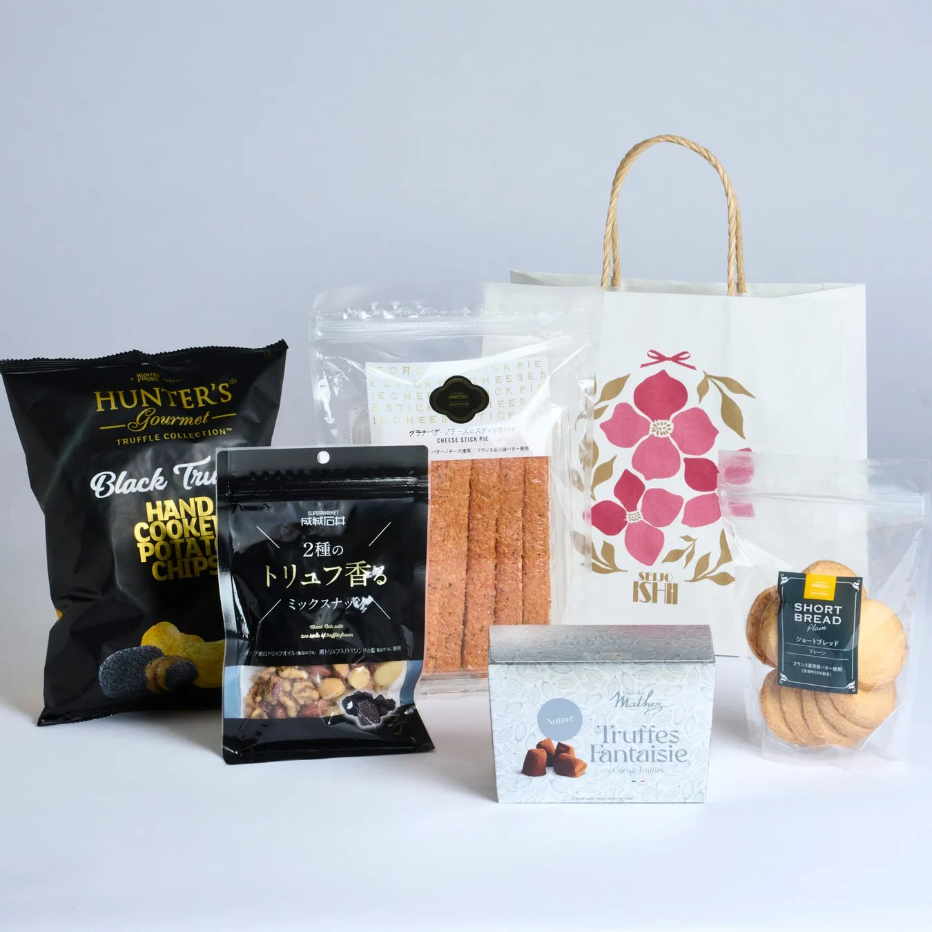 様々なお菓子や食品が写った写真。トリュフ風味のポテトチップスやナッツ、チーズスティックパイ、クッキー、トリュフチョコレート、そして手提げ袋が写っています。