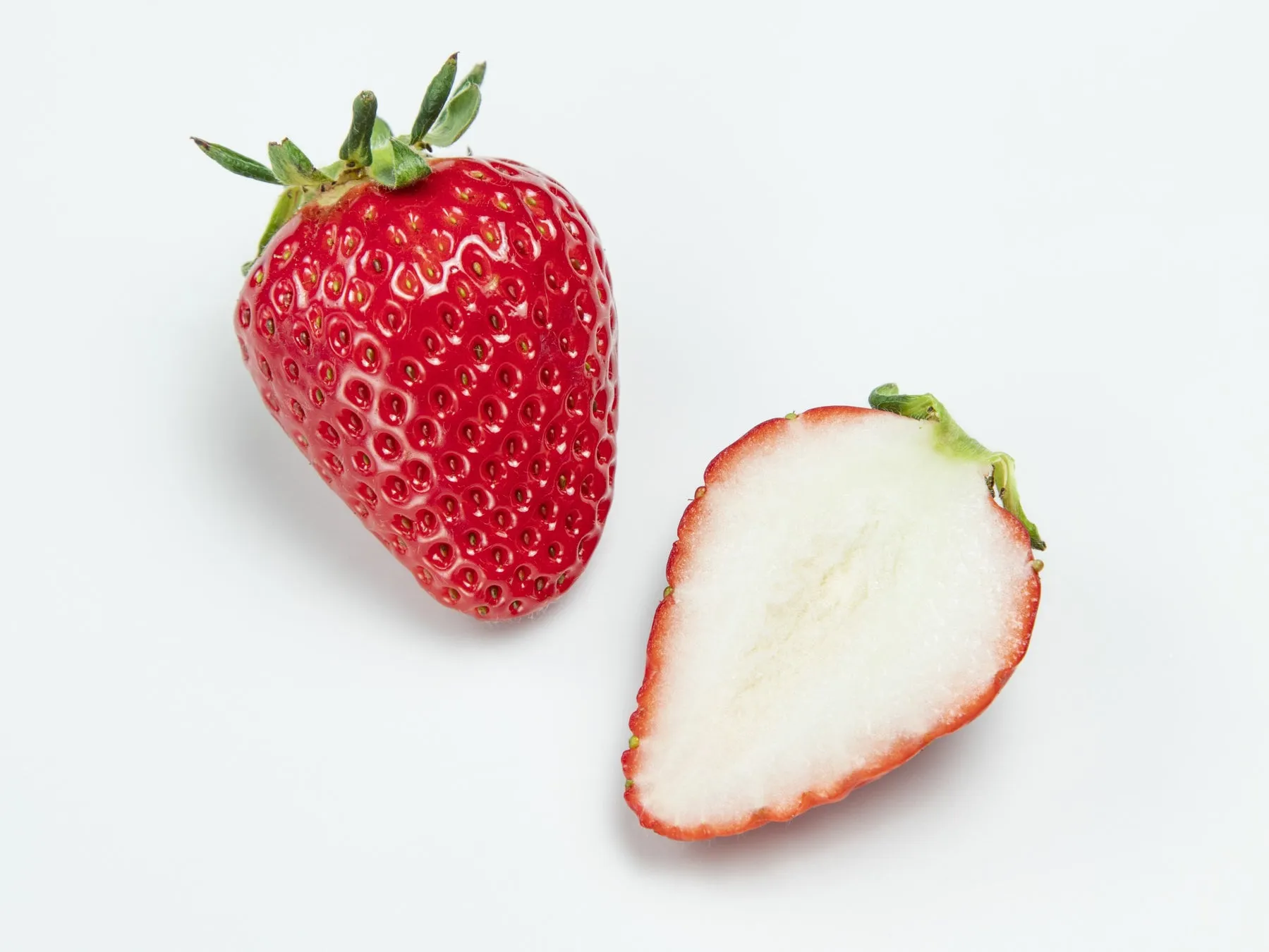 白い背景に、イチゴが2つ写っています。1つは丸ごとで、もう1つは半分にカットされています。