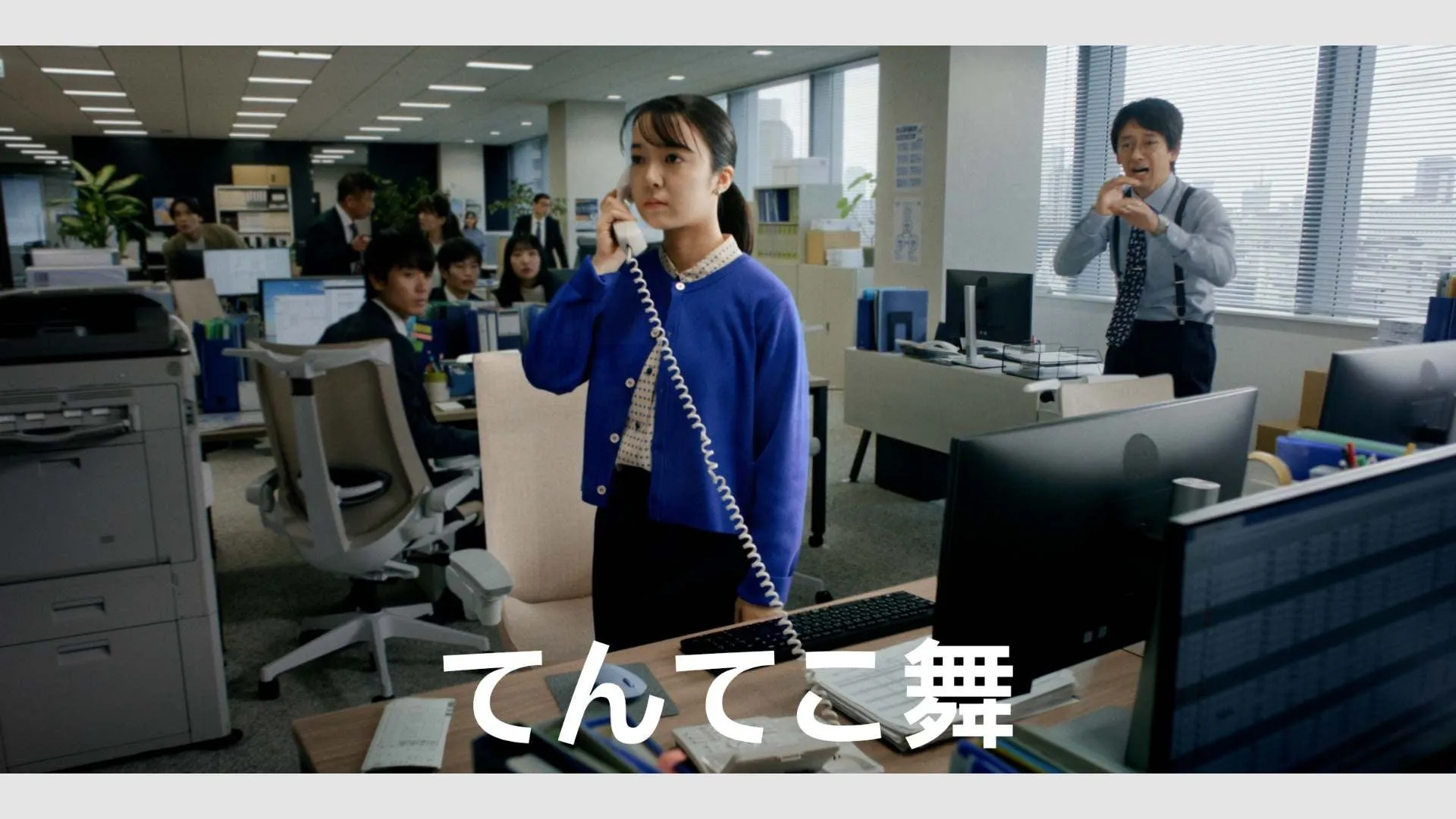 オフィスで電話をする女性と、驚いた表情の男性が描かれた写真。