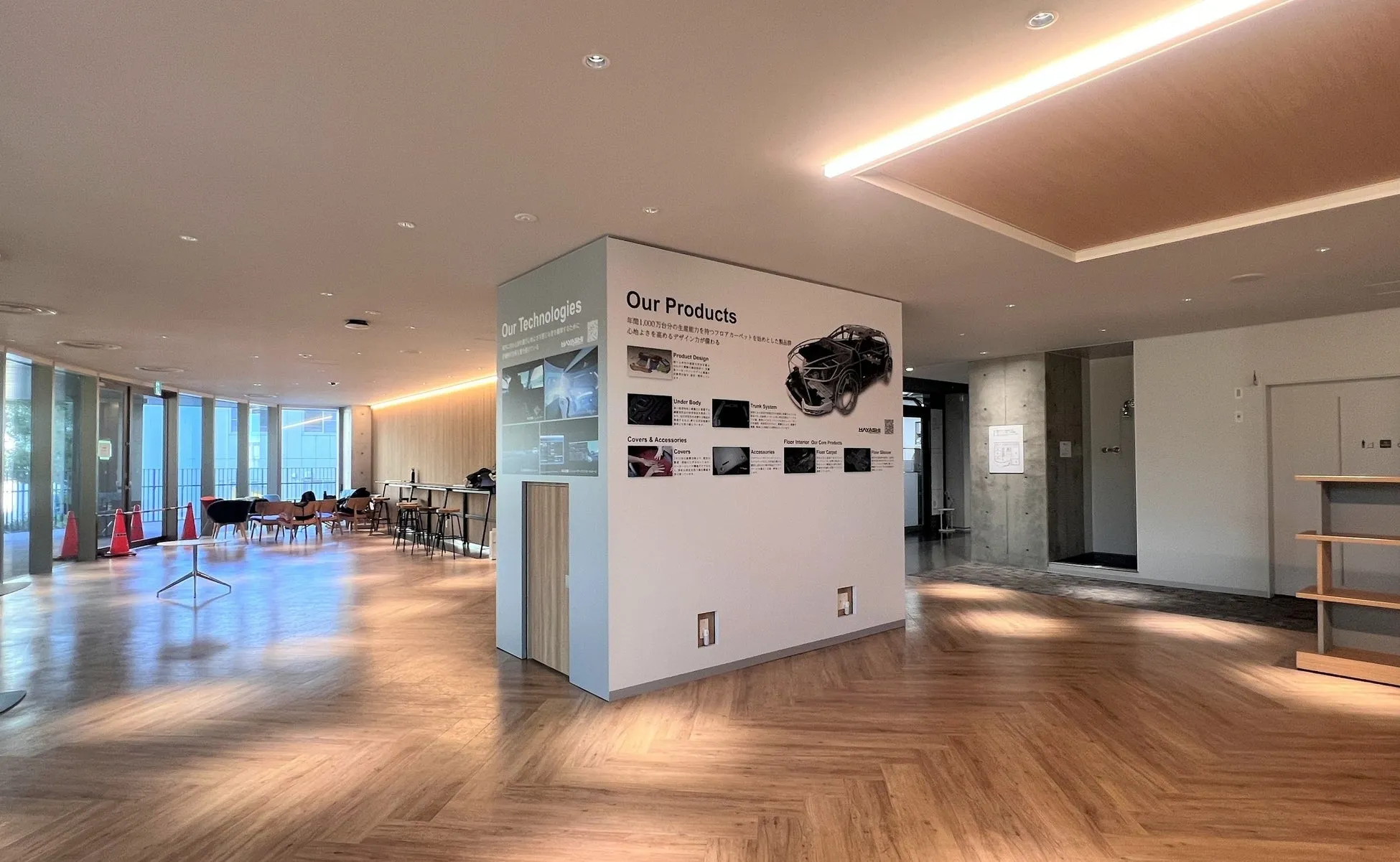 展示スペースの写真。壁には「Our Products」と「Our Technologies」の看板があり、製品デザイン、アンダーボディ、トランクシステム、カバーとアクセサリー、フロアインテリアなどが示されている。床は木目調。