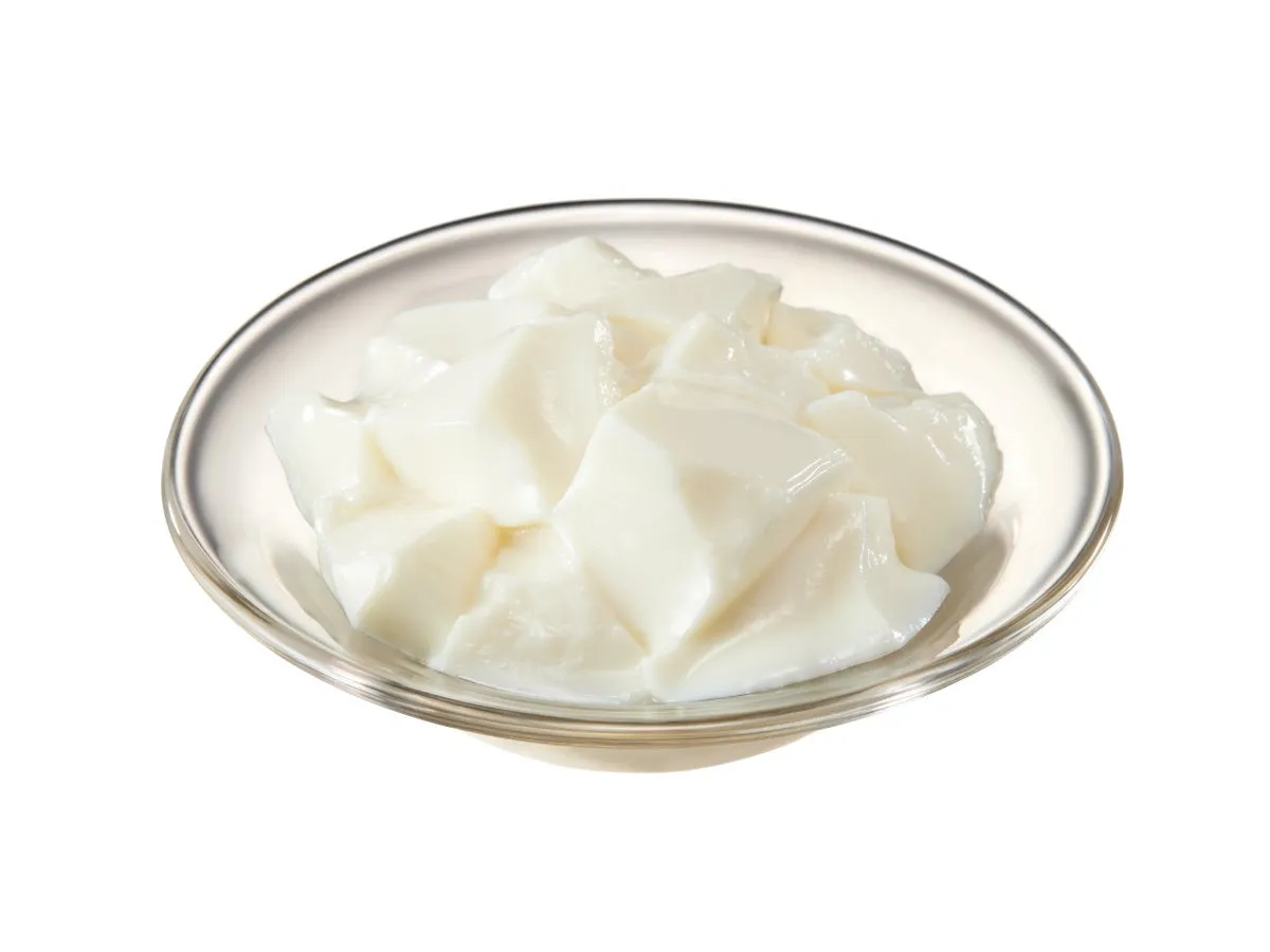 透明なガラスの器に入った白いデザートのクローズアップ写真です。デザートは、さいの目に切られたように見える、柔らかく角ばった塊で構成されています。