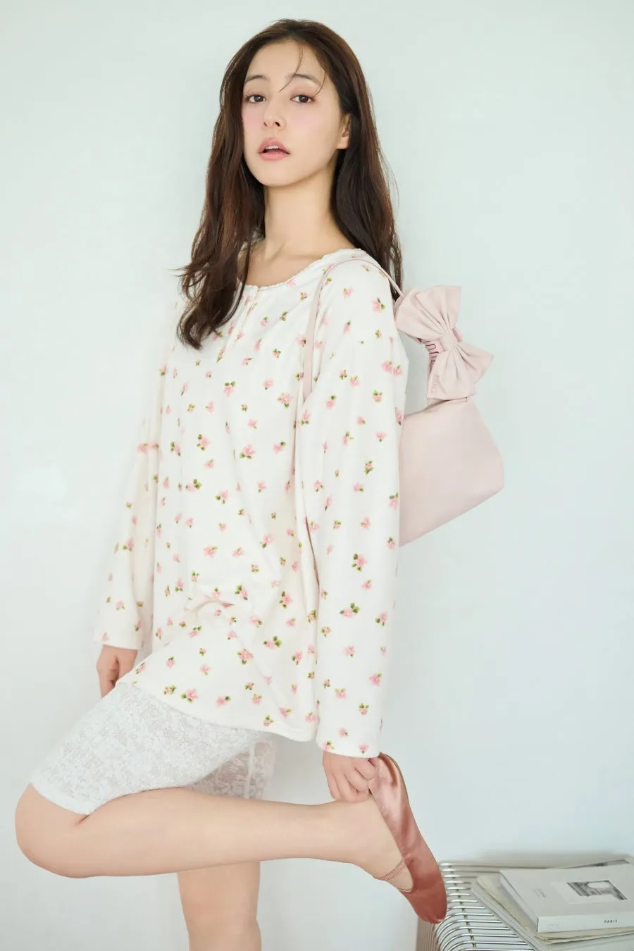 女性が花柄の長袖シャツと白いレースのショートパンツを着て、ピンクのバッグを肩にかけ、ピンクの靴を履いている写真です。