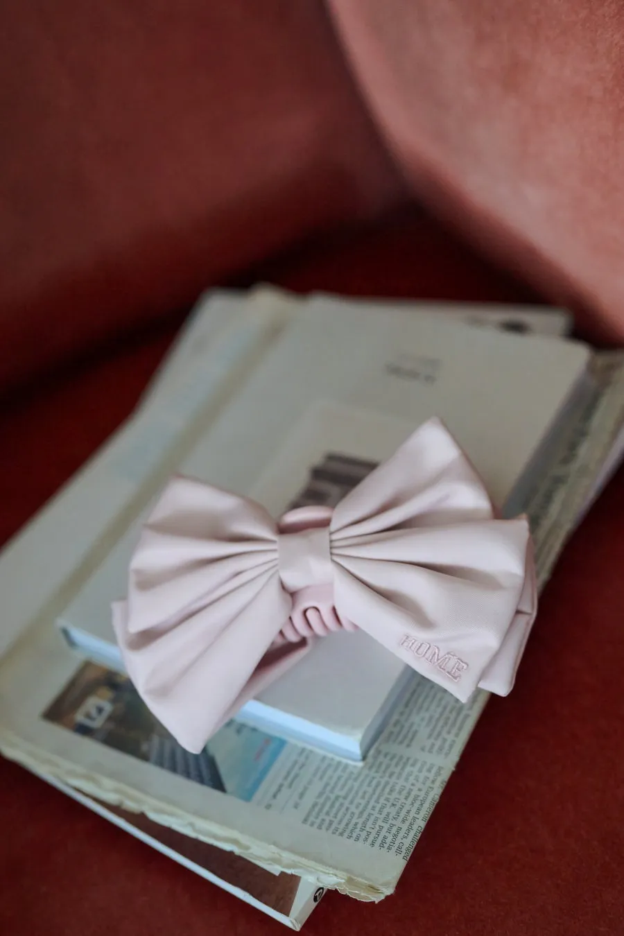 ピンク色のリボンが、新聞や本の上に置かれている写真です。「HOME」の文字が刺繍されています。