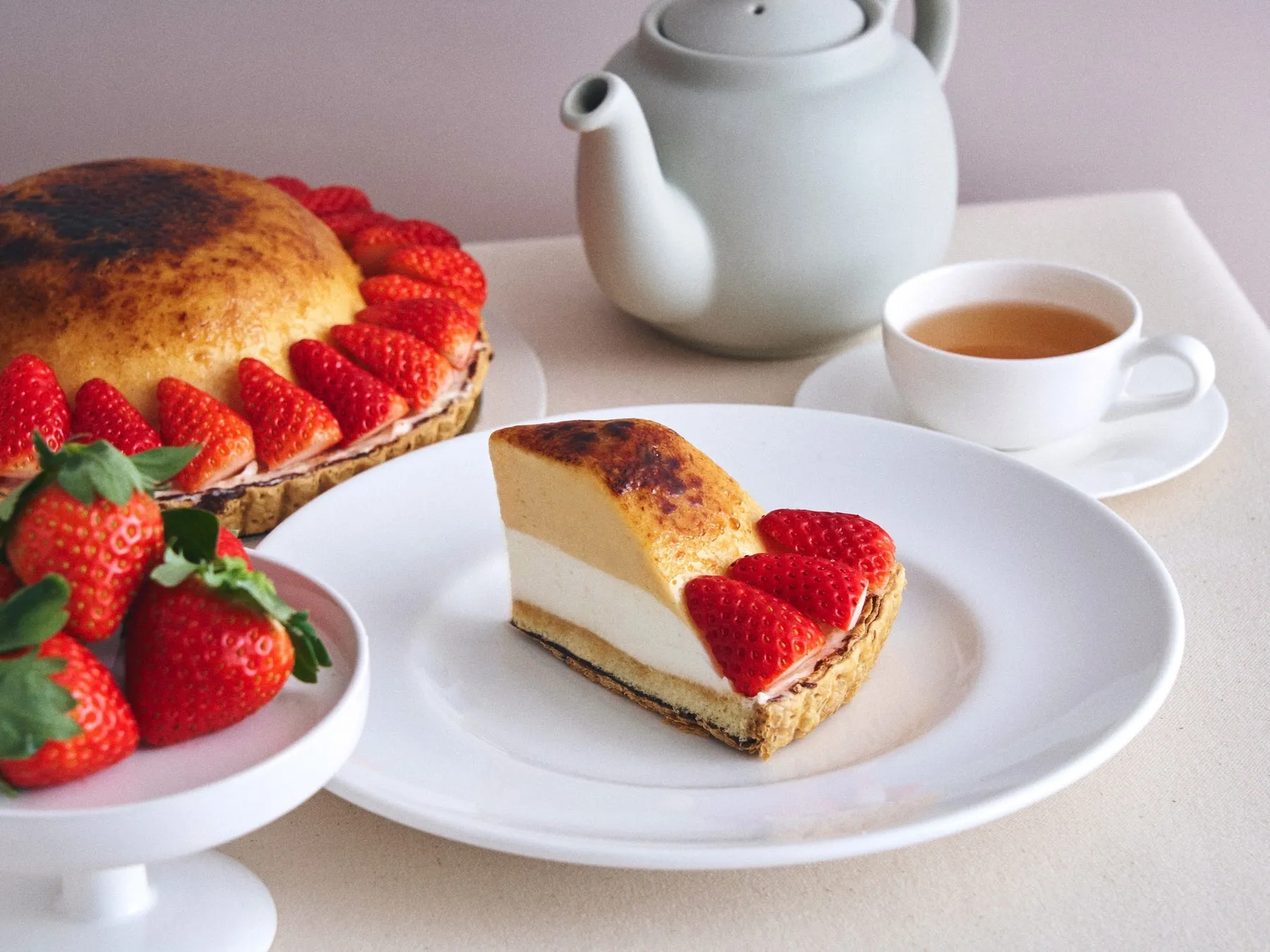 いちごのタルト、ケーキ、ティーカップ、ティーポットなど、テーブルの上に置かれた食べ物や食器を写した写真です。