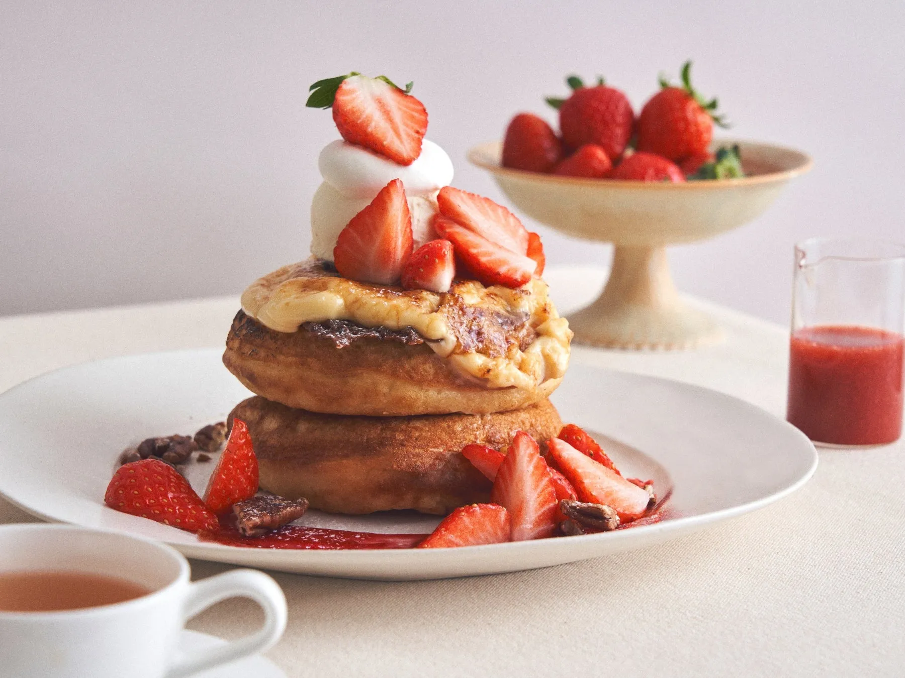 2段重ねのパンケーキに、クリームとイチゴがトッピングされ、イチゴソースとティーカップ、イチゴの盛り合わせが添えられた写真。