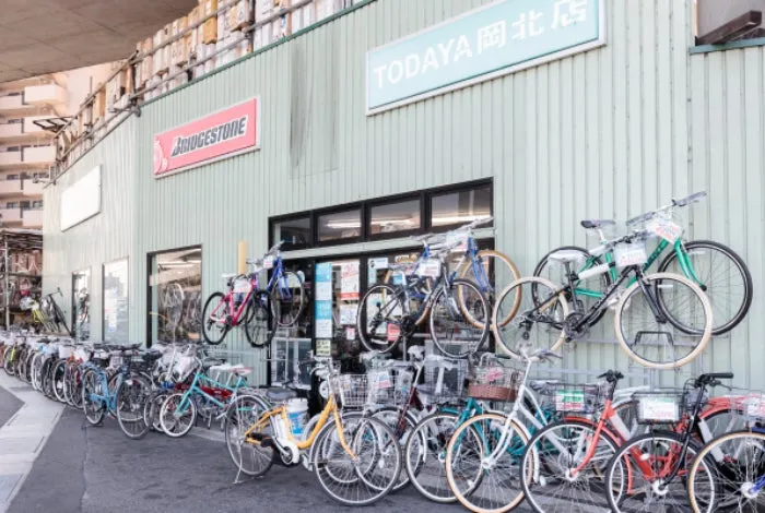 自転車販売店の外観写真。様々な種類の自転車が並べられ、店舗の看板には「TODAYA 岡北店」と「BRIDGESTONE」の文字が見える。
